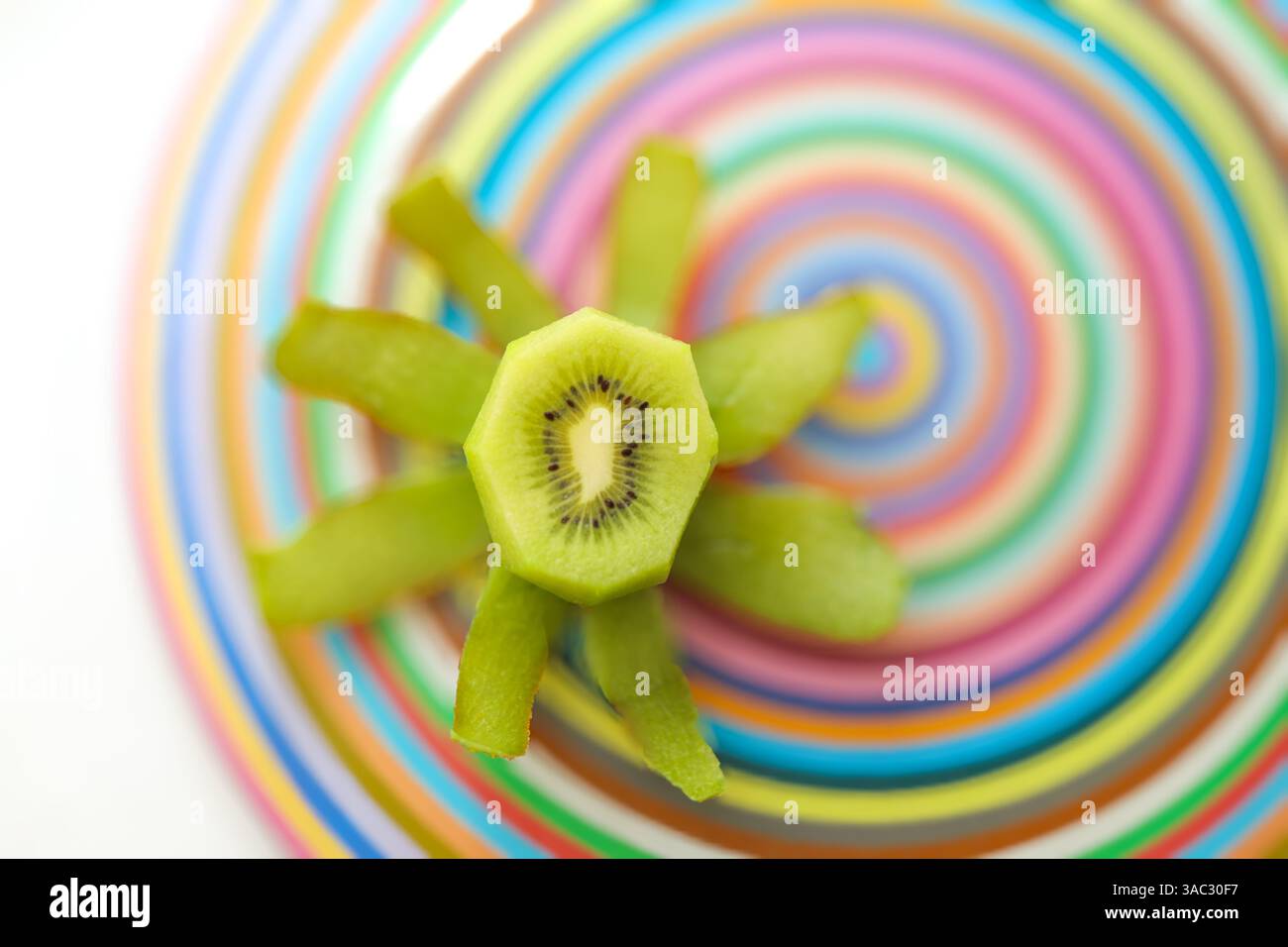 Geschälte Kiwis, die in einer Starburst auf einem farbenfrohen Schneidebrett aus Glas angeordnet sind, in Scheiben geschnitten, mit Samen und Saft Stockfoto