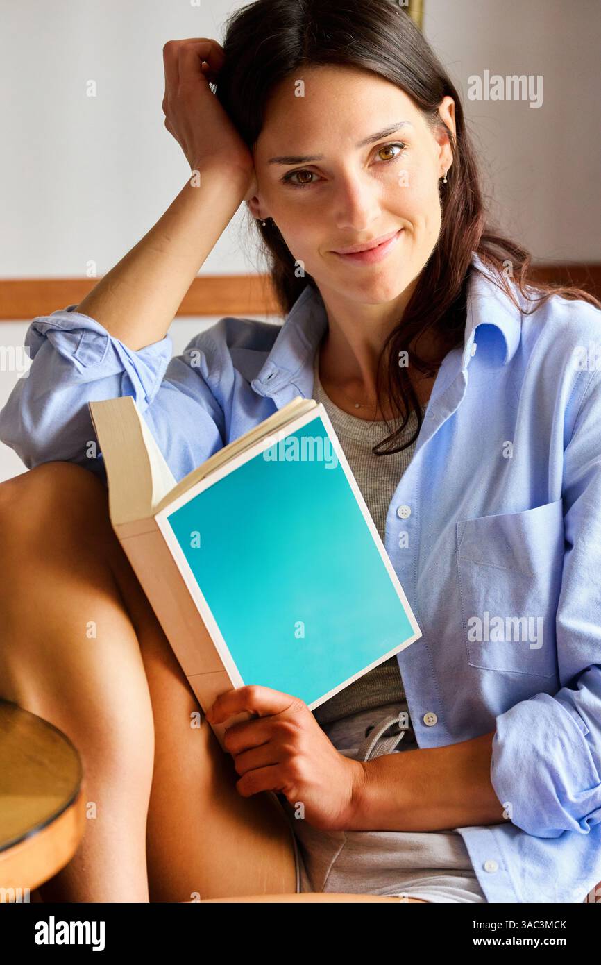 35-jährige Frau zu Hause, liest ein Buch, schaut in die Kamera Stockfoto