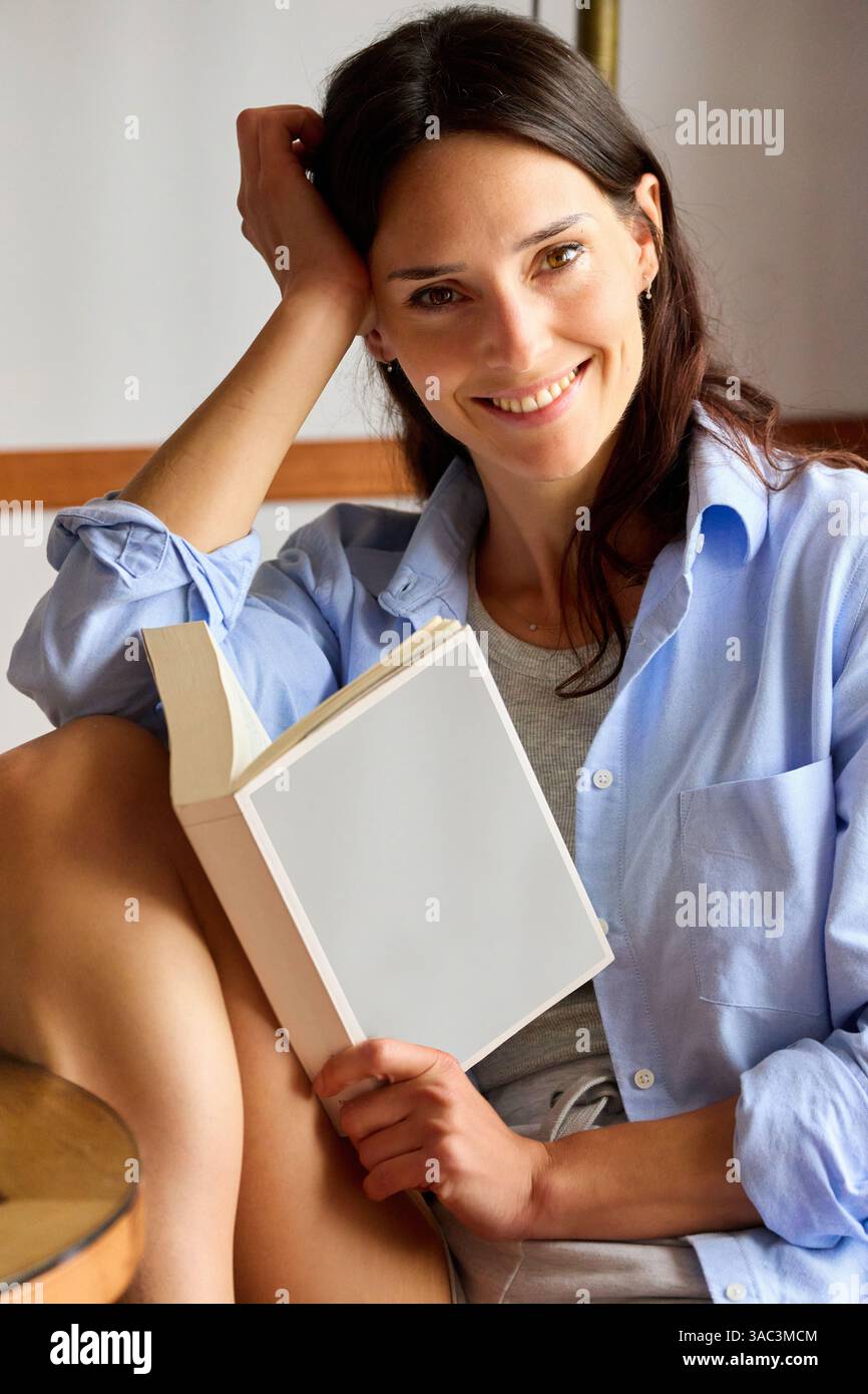 35-jährige Frau zu Hause, liest ein Buch, schaut in die Kamera Stockfoto