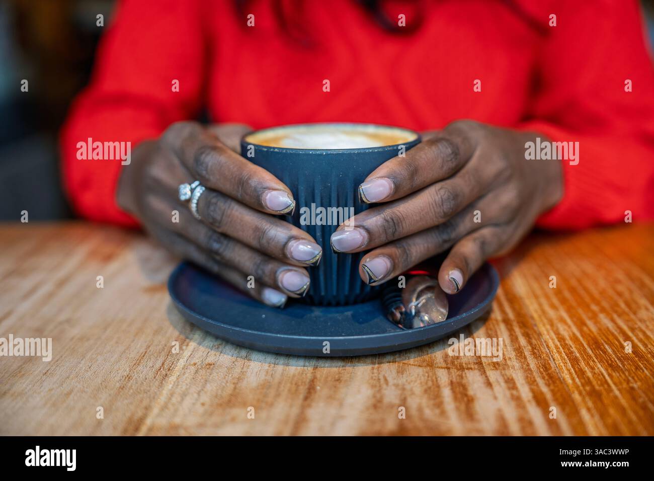 Die Hände legen eine Cappuccino-Tasse sanft in die Wiege und genießen einen ruhigen Moment in einem Café Stockfoto