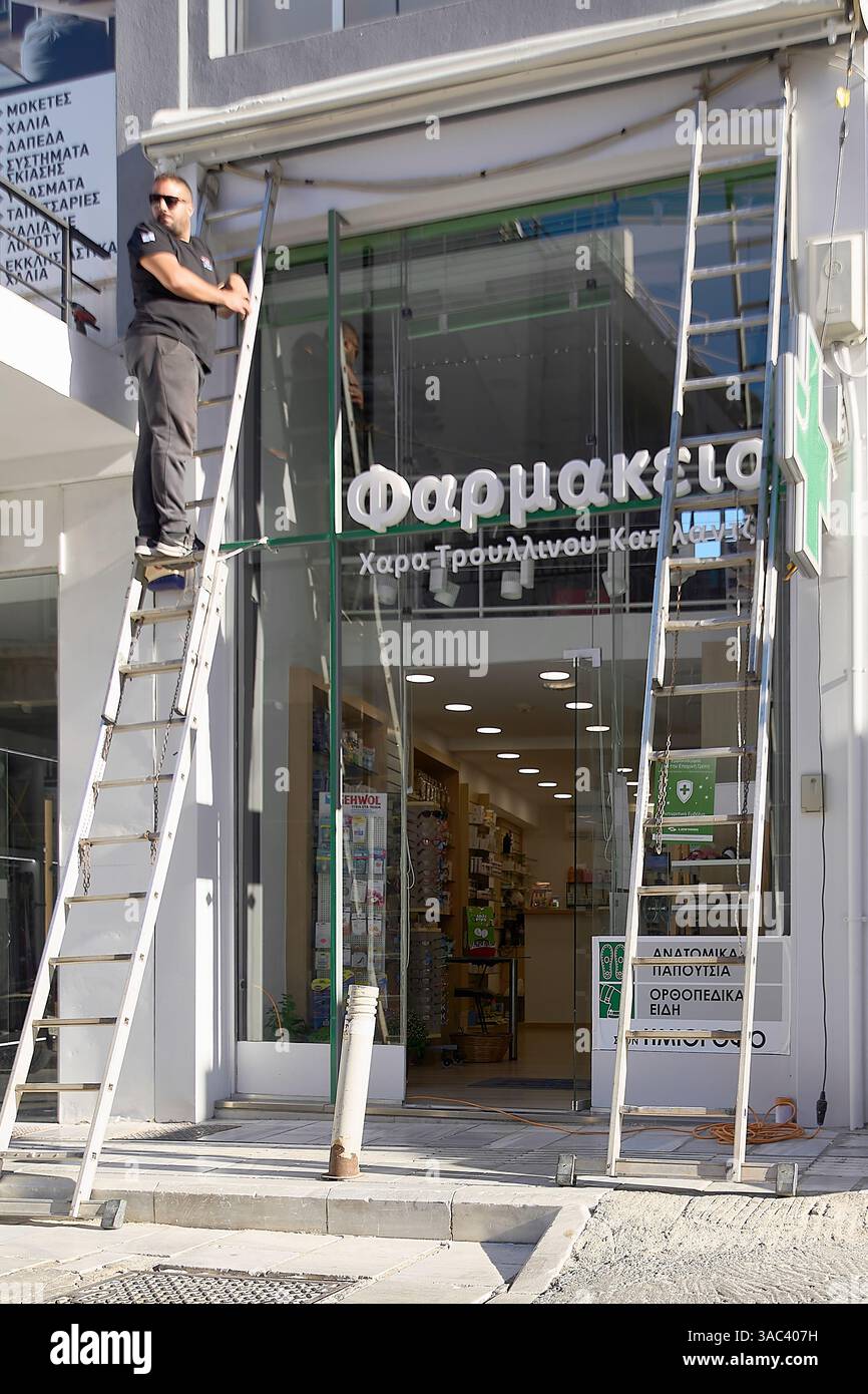Kreta. Griechenland - 03. april 2025: Eingang der griechischen Apotheke mit Beschilderung und sichtbaren Wartungsarbeiten, grünes Kreuz-Symbol und sortierten Regalen Stockfoto