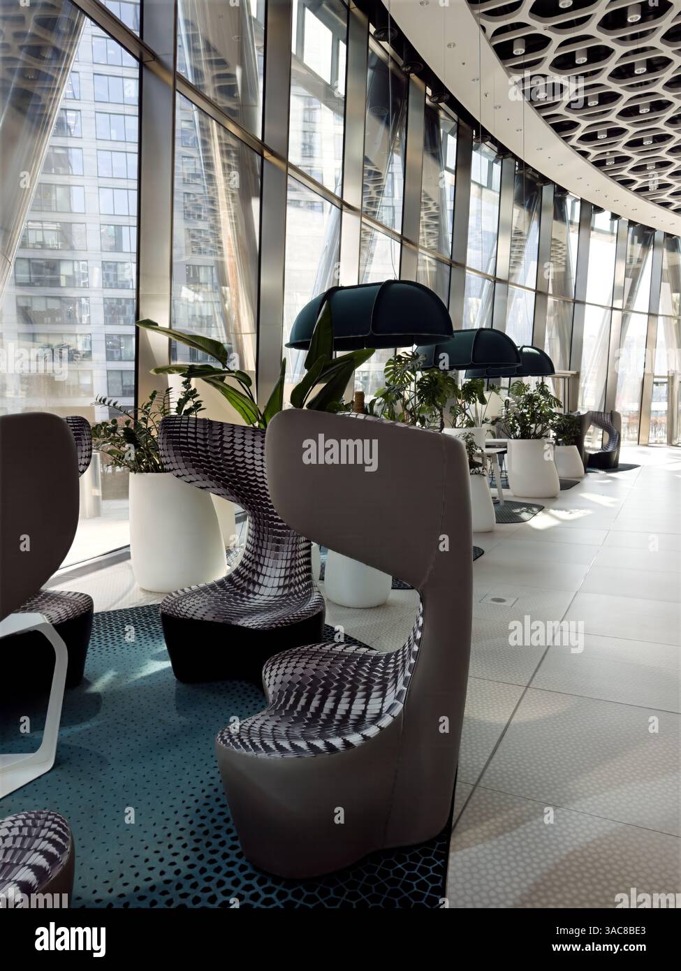 Coworking Space mit futuristischen Stühlen, Panoramafenstern und üppigen Innenpflanzen. Moderne Inneneinrichtung mit Tageslicht und eleganter Einrichtung. - Smartphone-aufgenommenes Stockfoto