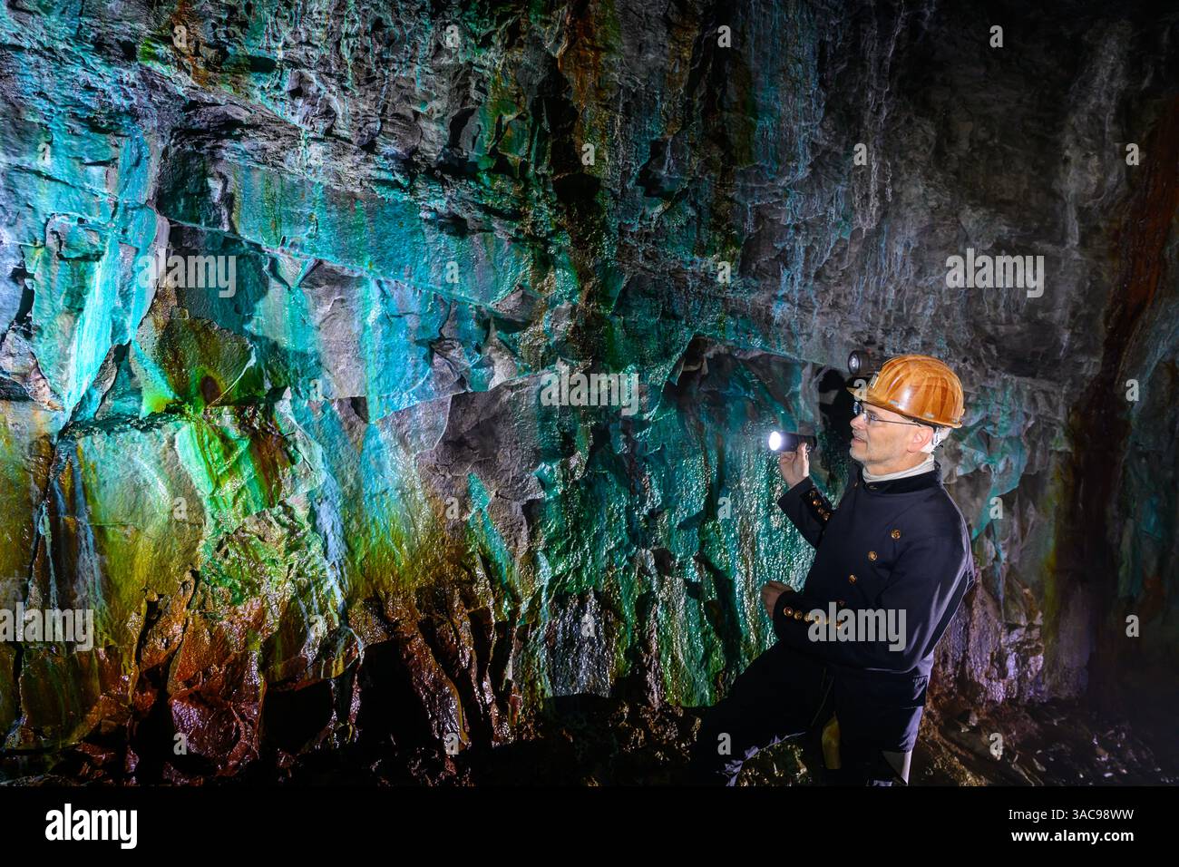 PRODUKTION - 02. April 2025, Sachsen-Anhalt, Sangerhausen: Thomas Wäsche, Leiter des Erlebniszentrums Bergbau Röhrigschacht Wettelrode, steht fast 300 Meter unterirdisch im sogenannten Grünen Gewölbe. Das Sintern wird durch gelöste Mineralien aus dem Kalkstein verursacht. Die Farbpalette reicht von kräftigen Brauntönen bis zu weiß, Grün, Türkis, Blau und Schwarz. Die ersten Bergleute begannen vor 825 Jahren in der Region Mansfeld mit dem Graben nach Kupfererz. Ab 1750 wurde ein intensiver Bergbau durchgeführt. Insgesamt wurden rund 2,6 Millionen Tonnen Kupfer und 14.213 Tonnen Silber aus dem Erz gewonnen Stockfoto