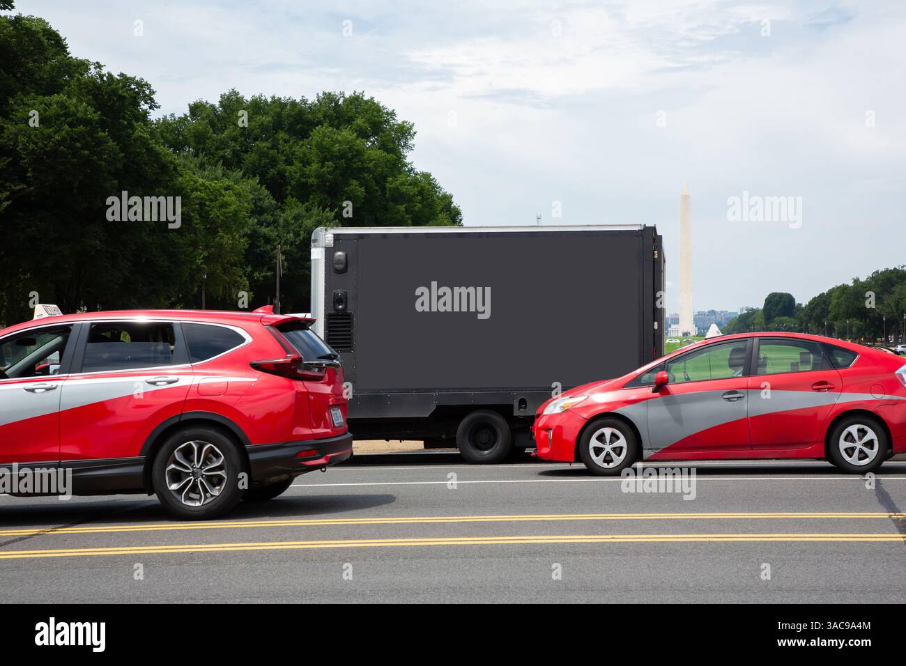 Zwei rote Fahrzeuge stehen am Straßenrand mit Blick auf eine grüne Kulisse und ein markantes Denkmal in Washington D.C. es ist ein sonniger Tag mit klarer Sicht Stockfoto