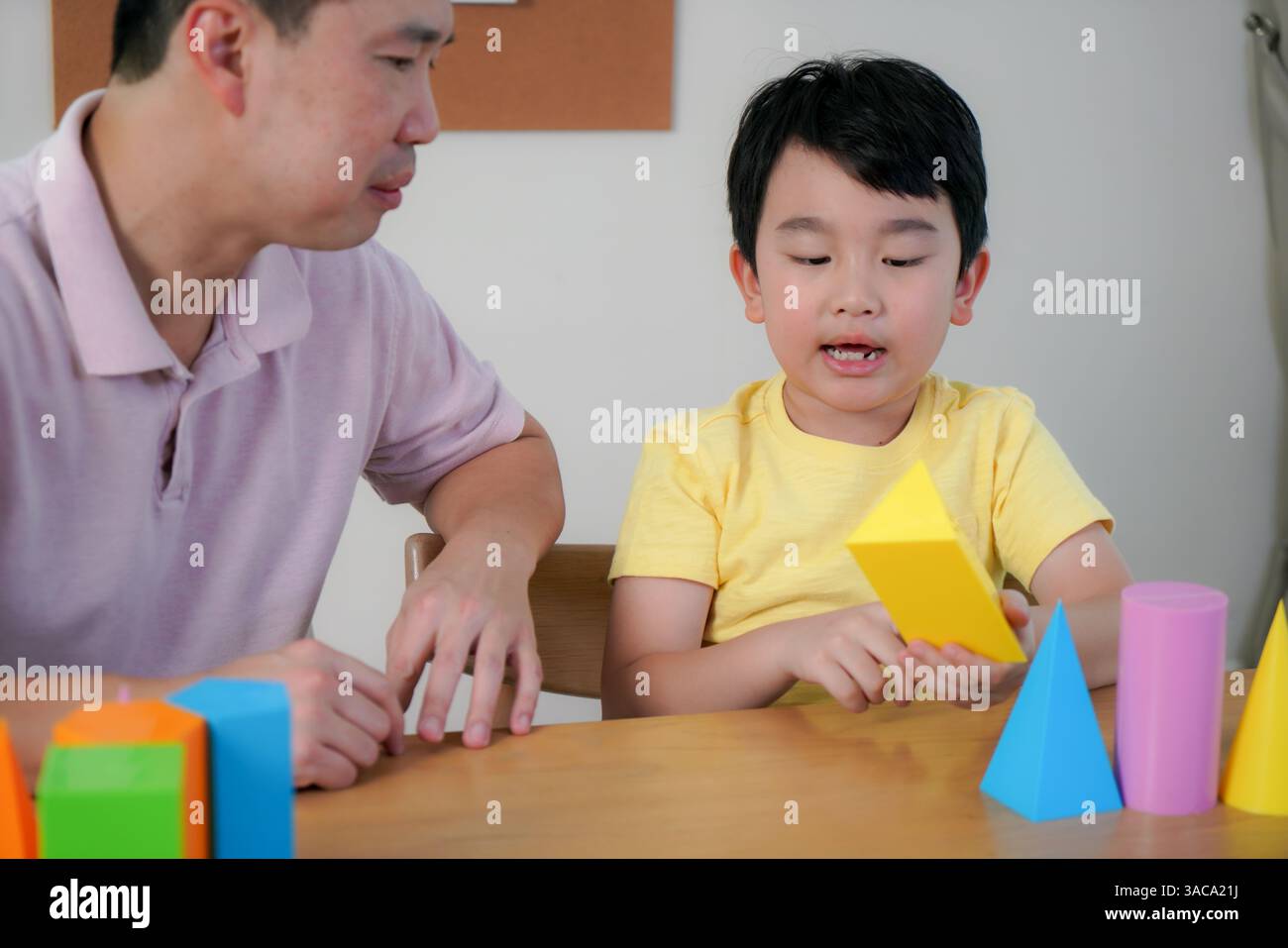 Vater führt seinen Sohn mit einer hellen Kegelform, die Kreativität und frühes Lernen in einer entspannten häuslichen Umgebung weckt. Stockfoto