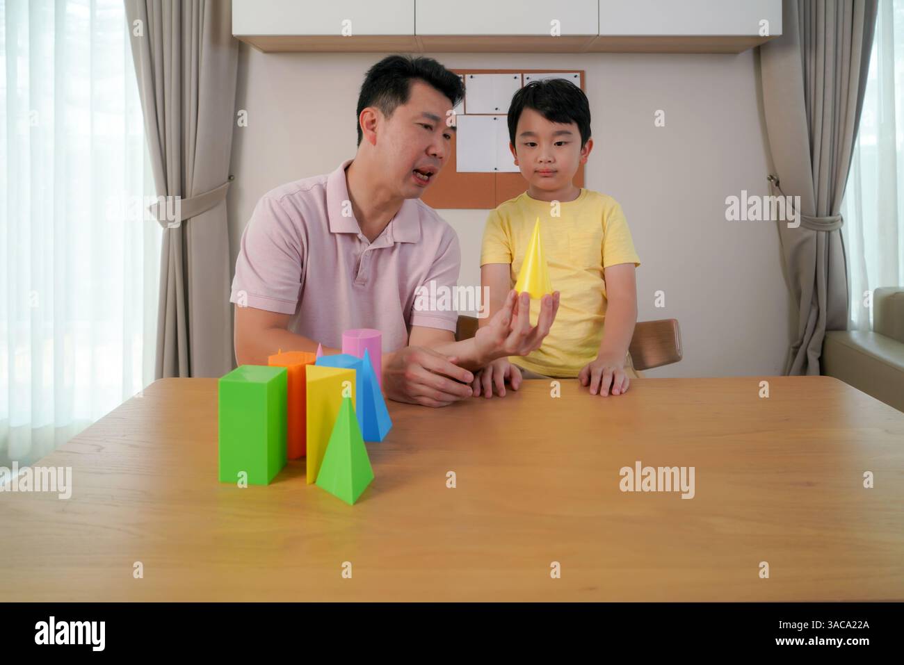 Vater führt seinen Sohn mit einer hellen Kegelform, die Kreativität und frühes Lernen in einer entspannten häuslichen Umgebung weckt. Stockfoto