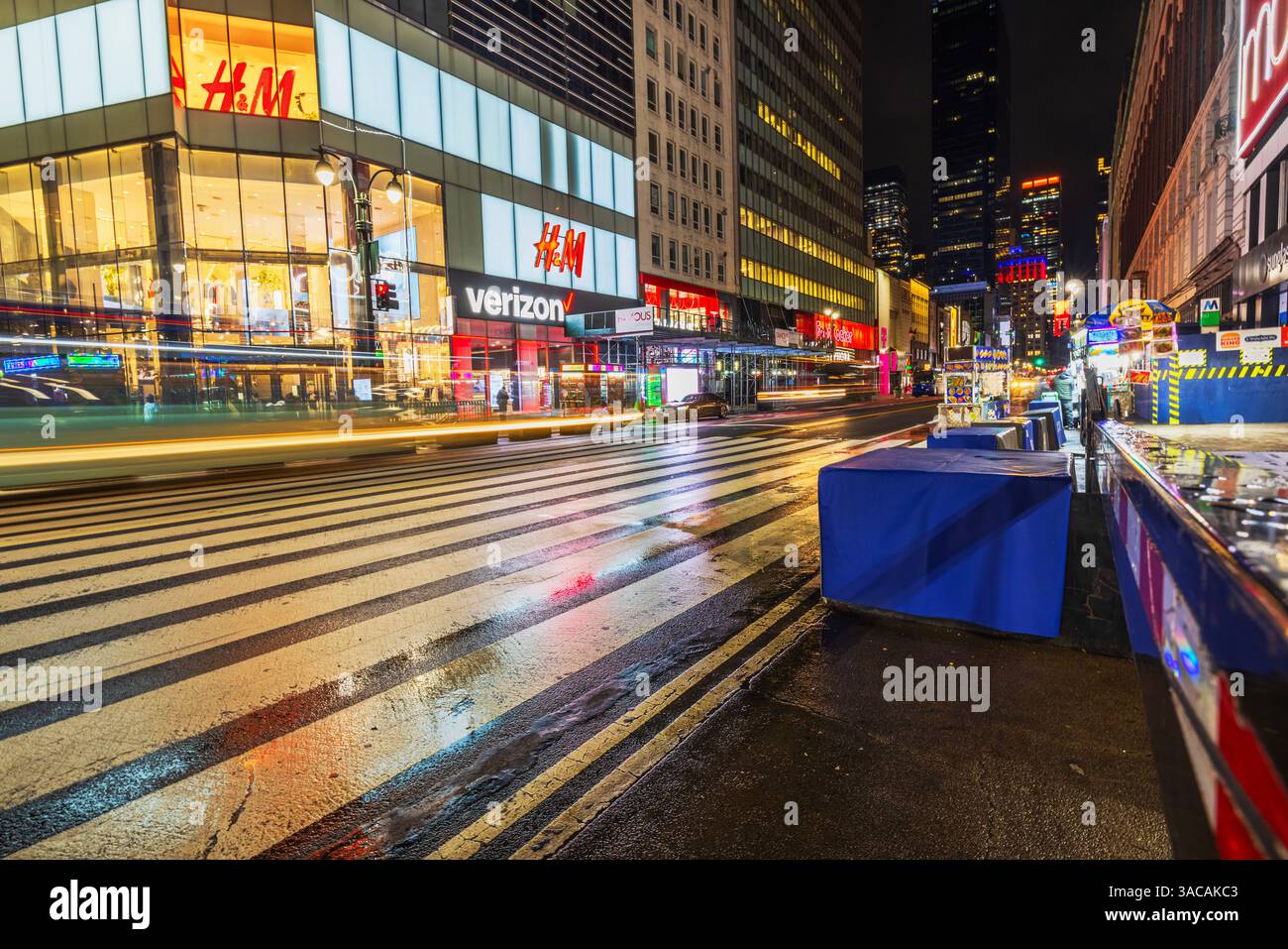 Crosswalk bei Nacht in Manhattan mit leuchtenden Ladenfronten, verschwommenen Lichtern und Reflexionen nach Regen. New York. USA. Stockfoto