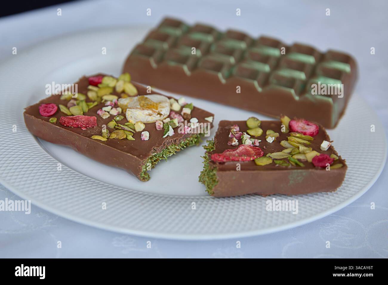 Dubai Schokolade. Exquisite handgefertigte Schokolade, elegant garniert mit zerstoßenen Pistazien, hellen Himbeerstücken und ätherischer Schlagsahne, EV Stockfoto