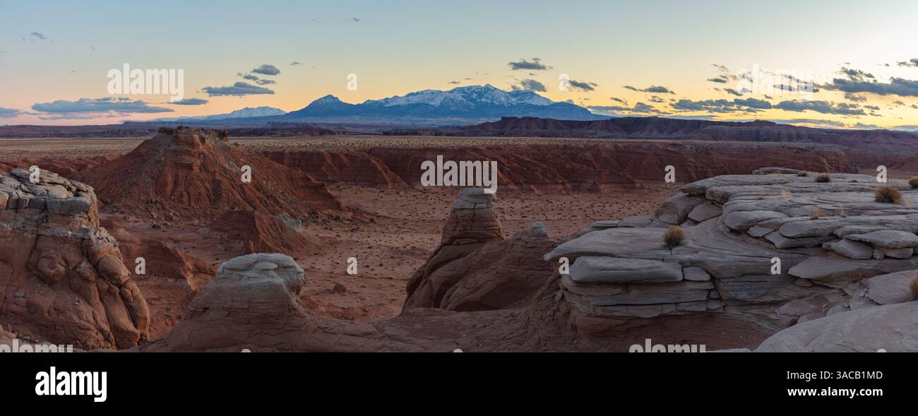 Ein malerischer Canyon in den Utah Badlands bei Sonnenuntergang mit den schneebedeckten Henry Mountains umgeben von bunten Wolken, die sich in der Ferne erheben. Stockfoto