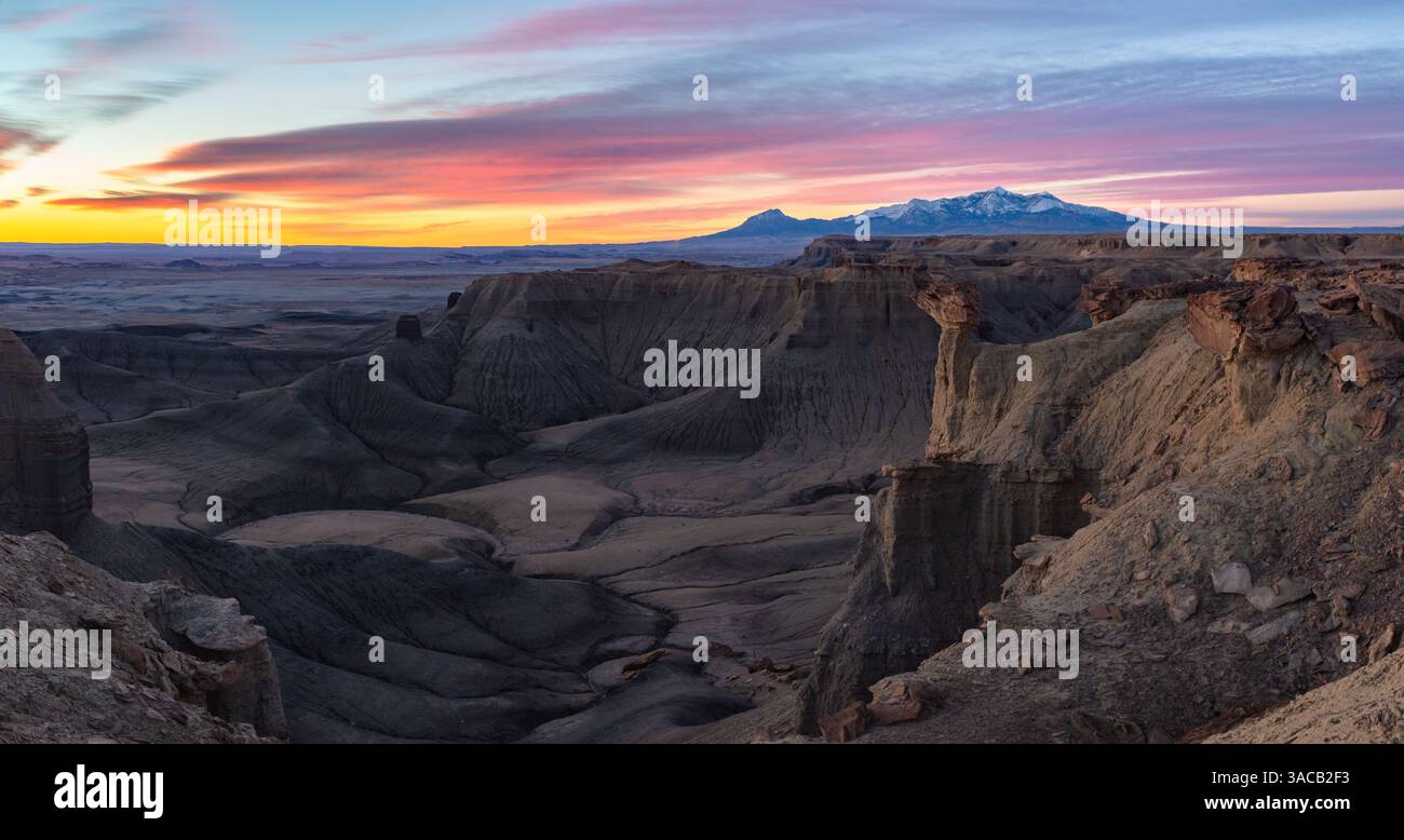 Dieses farbenfrohe Panorama bei Sonnenaufgang zeigt die zerklüfteten Utah Badlands und die schneebedeckten Henry Mountains in der Nähe von Hanksville. Stockfoto