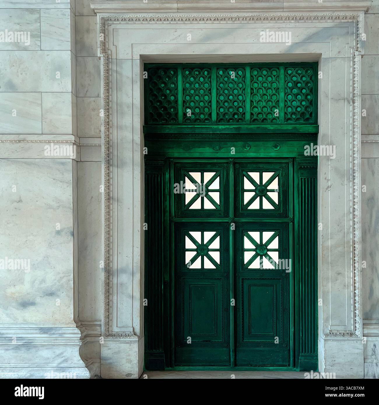 Eine grüne Tür mit geometrischen Glaspaneelen und dekorativen Grilleworks ist in einem kunstvollen Marmorrahmen untergebracht, der neoklassizistische Eleganz veranschaulicht. - Smartphone-aufgenommenes Stockfoto