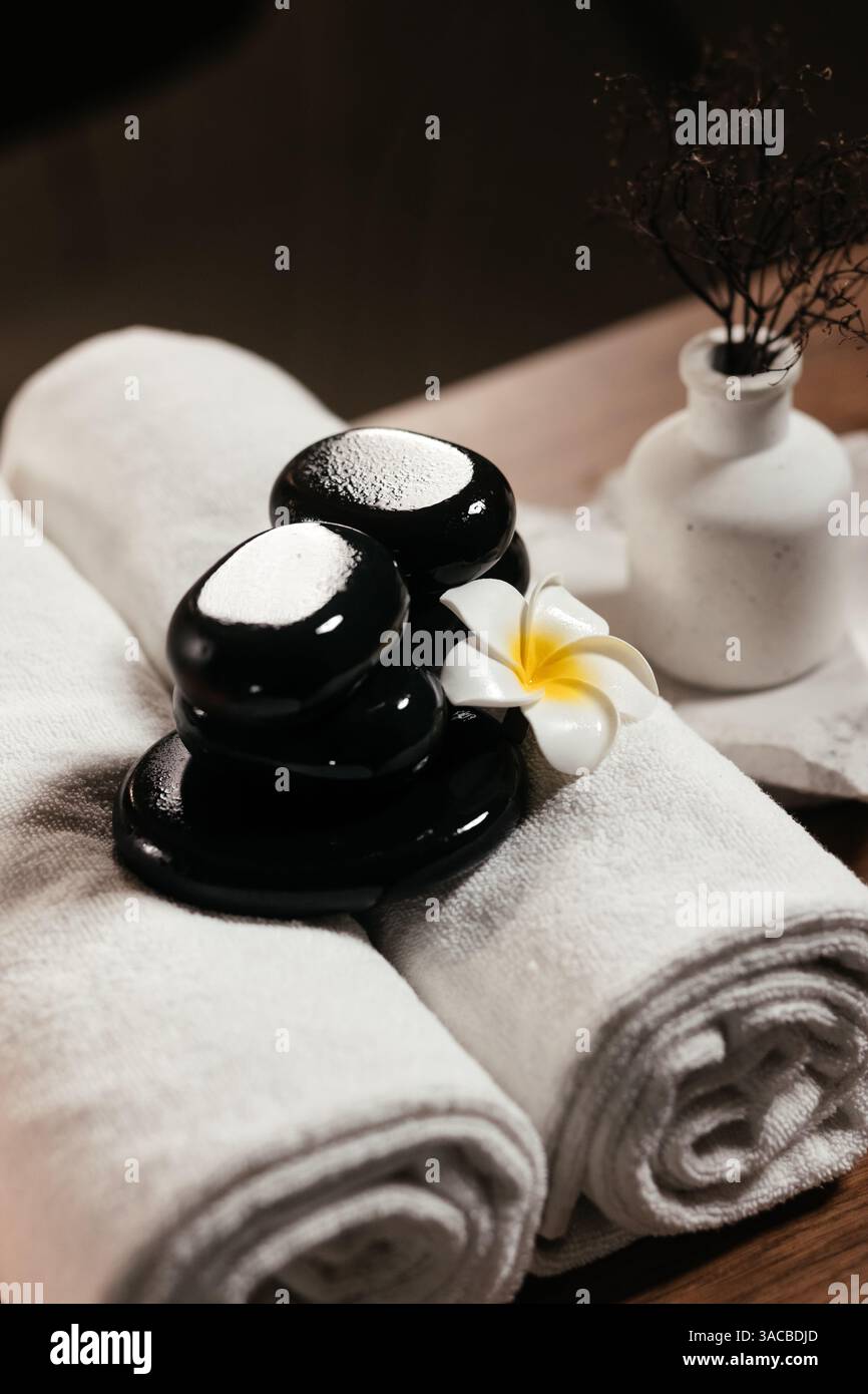 Komposition mit weißen Handtüchern, Frangipani-Blume und heißen Steinen für Massage im Spa-Salon. Spa, Beauty-Behandlung und Wellness-Konzept Hintergrund Stockfoto