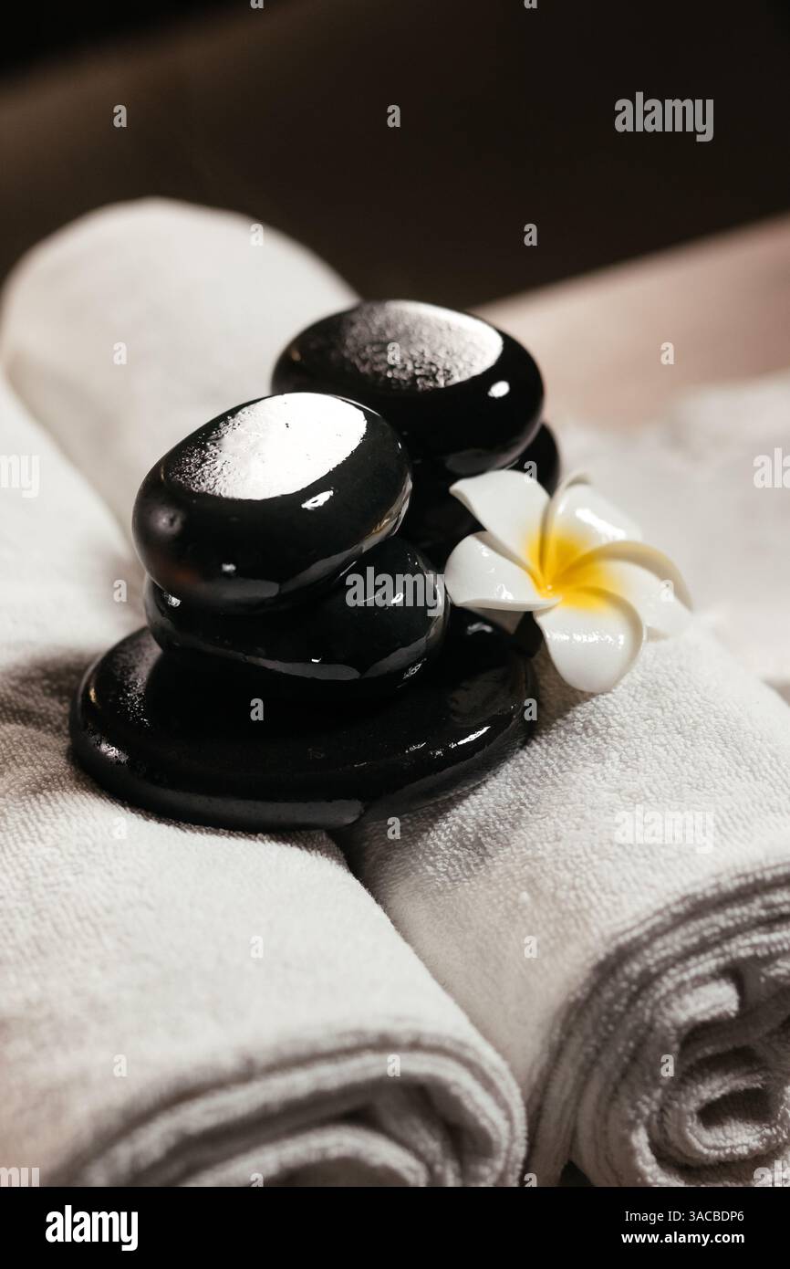 Komposition mit weißen Handtüchern, Frangipani-Blume und heißen Steinen für Massage im Spa-Salon. Spa, Beauty-Behandlung und Wellness-Konzept Hintergrund Stockfoto