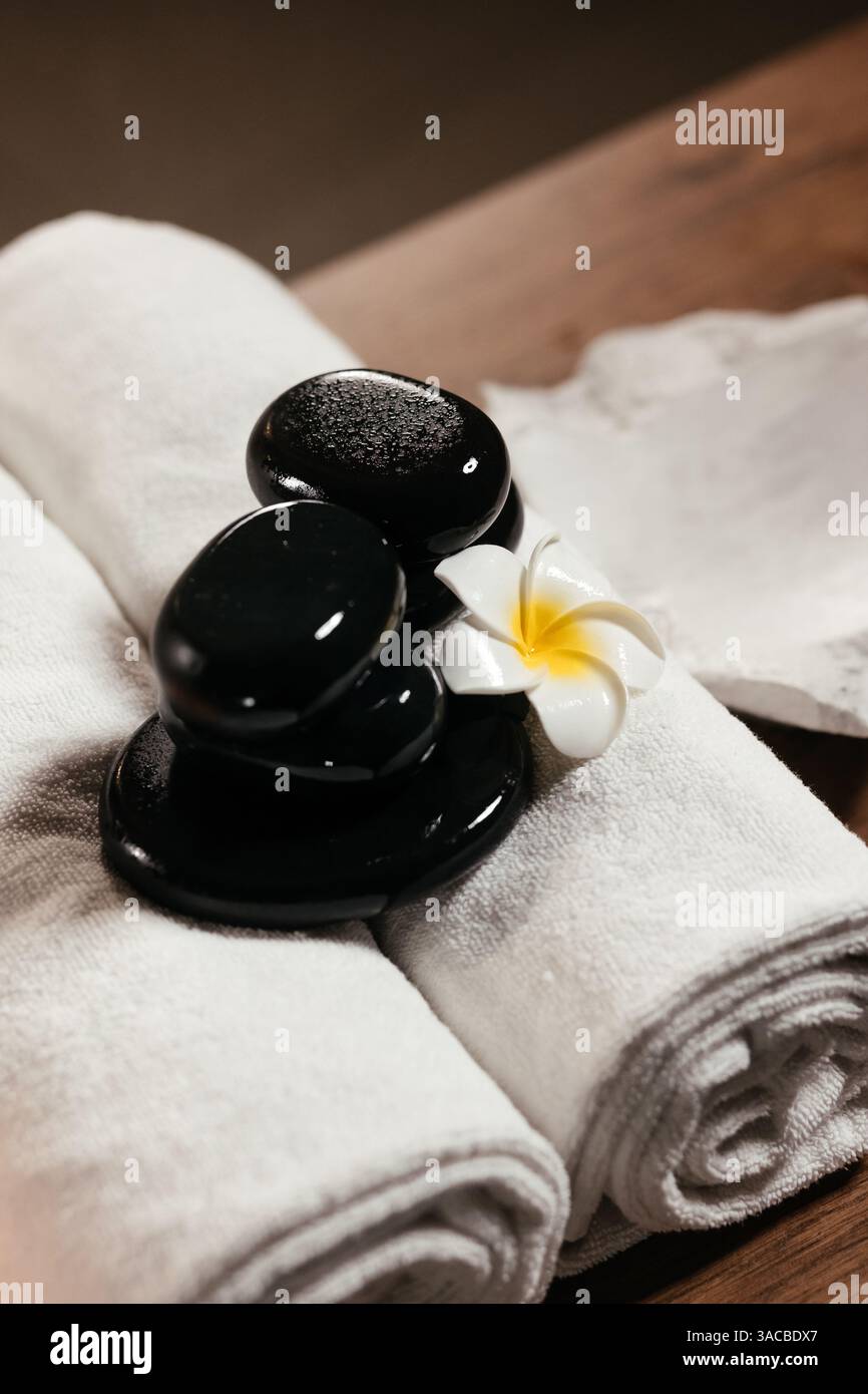 Komposition mit weißen Handtüchern, Frangipani-Blume und heißen Steinen für Massage im Spa-Salon. Spa, Beauty-Behandlung und Wellness-Konzept Hintergrund Stockfoto