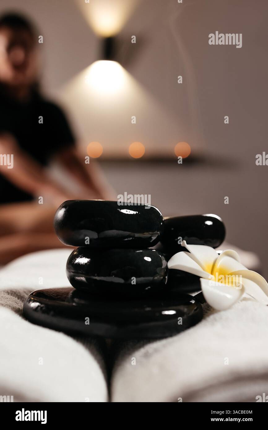 Komposition mit weißen Handtüchern, Frangipani-Blume und heißen Steinen für Massage im Spa-Salon. Spa, Beauty-Behandlung und Wellness-Konzept Hintergrund Stockfoto