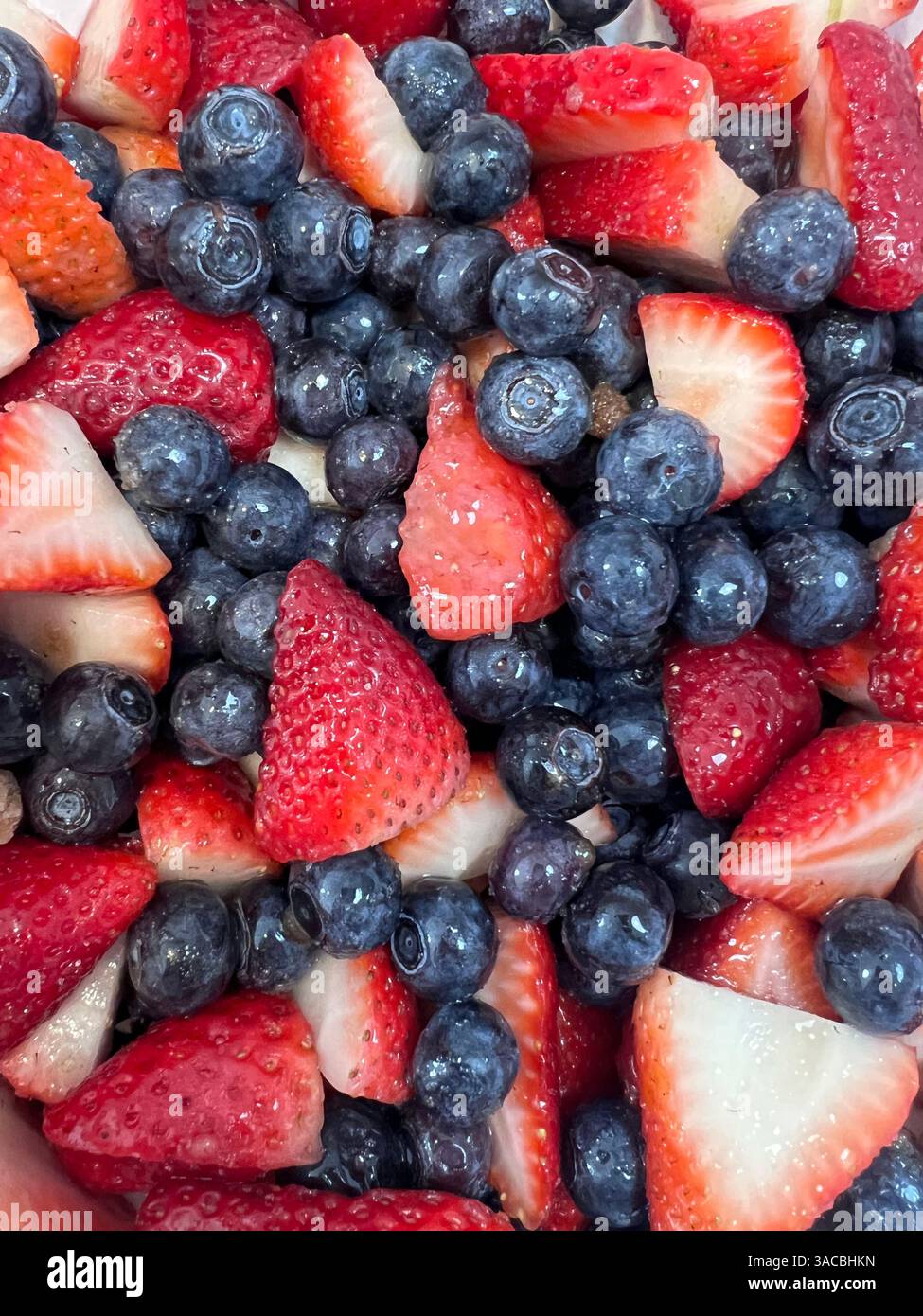 Frisch geschnittene Erdbeeren und Heidelbeeren, die zusammen für einen gesunden Snack oder ein Dessert zubereitet werden Stockfoto