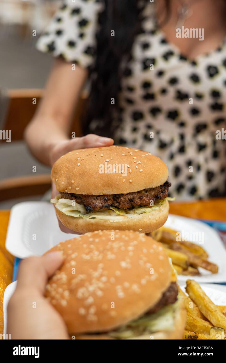 Zwei Personen genießen Burger und Pommes Frites, ihre Hände greifen nach Essen in einem zwanglosen, gemeinsamen Moment voller Geschmack und Verbundenheit. Stockfoto