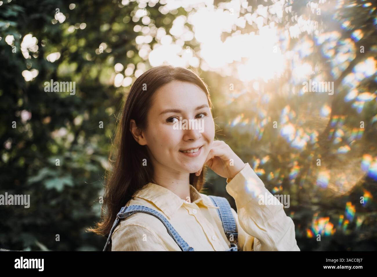 Junge Frau mit hellerer Haut und braunem Haar, die sanft in einer sonnendurchfluteten Umgebung im Freien lächelt. Positive Einstellung, emotionales Wohlbefinden, Selbstakzeptanz, persönlich Stockfoto