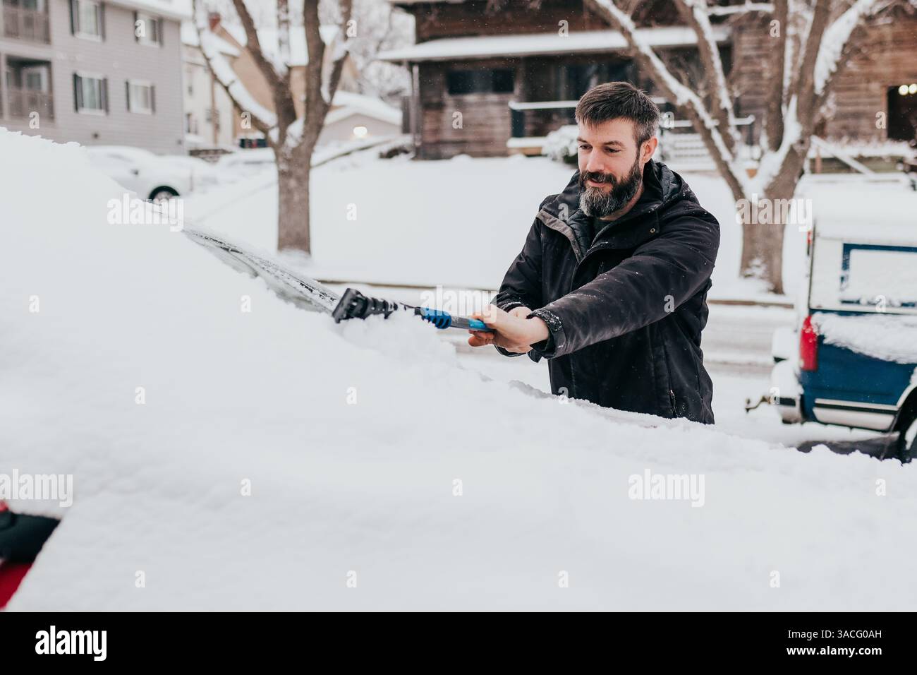 Der Mensch reinigt den Schnee am frühen Morgen nach Schneesturm vom Auto Stockfoto