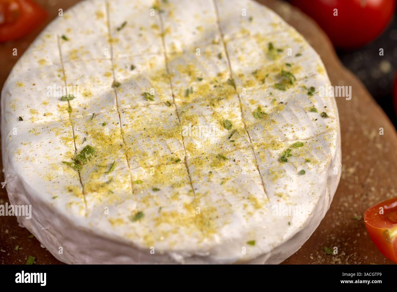 Weißer Weichkäse in Salz und Gewürzen und kleine rote runde Tomaten auf dem Tisch, Nahaufnahme, Blick von oben Stockfoto