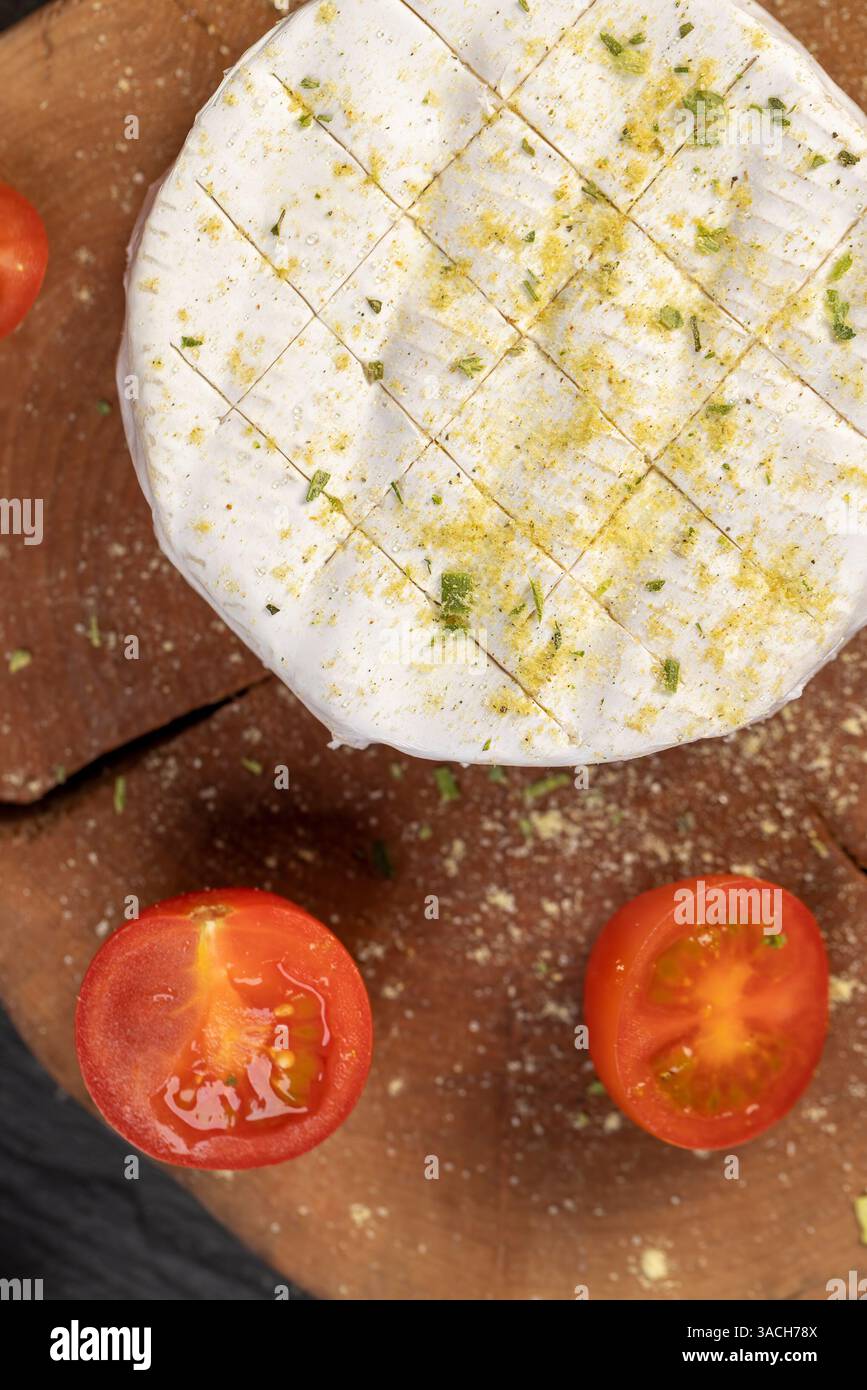 Weichkäse mit Schimmelpilz bestreut mit Gewürzen und Reifen kleinen roten Tomaten, weißer Weichkäse in Salz und Gewürzen und kleine rote runde Tomaten auf dem Tisch Stockfoto
