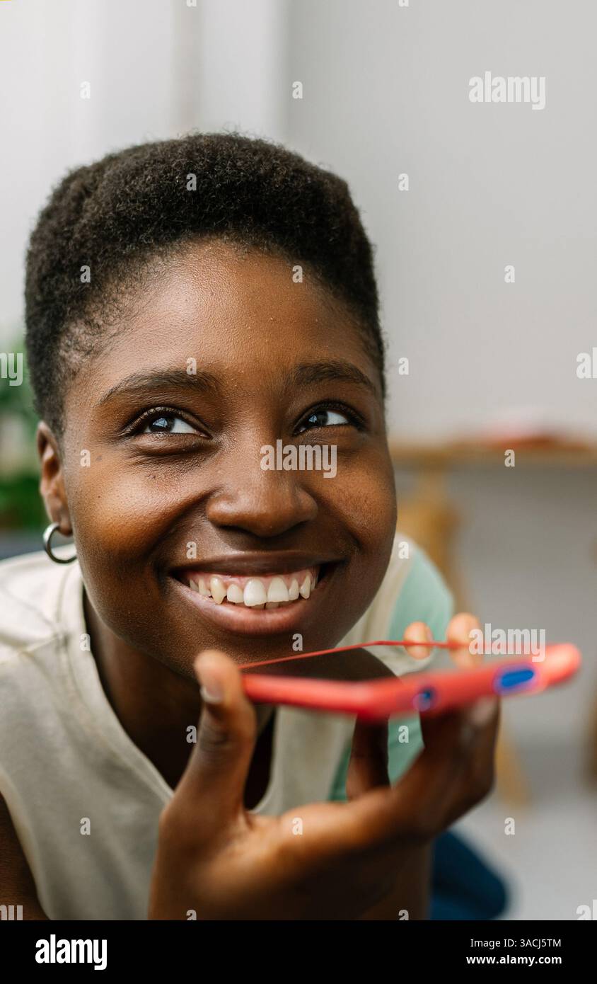 Glückliche schwarze Frau, die zu Hause den Sprachassistenten auf dem Smartphone benutzt Stockfoto