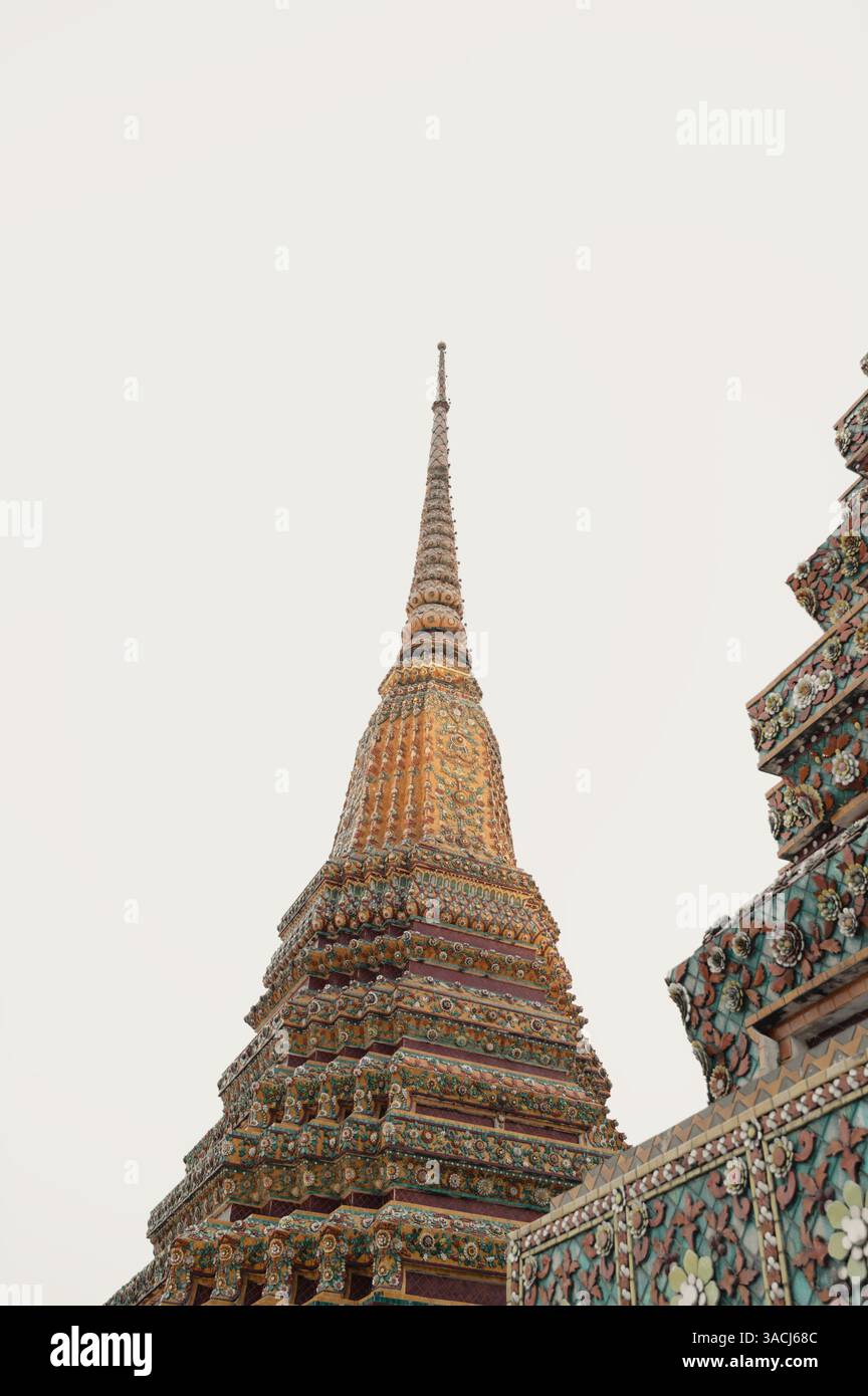 Im Wat Pho erheben sich goldene Türme in einen hellen Himmel, gekrönt von zarten Keramikblüten Stockfoto