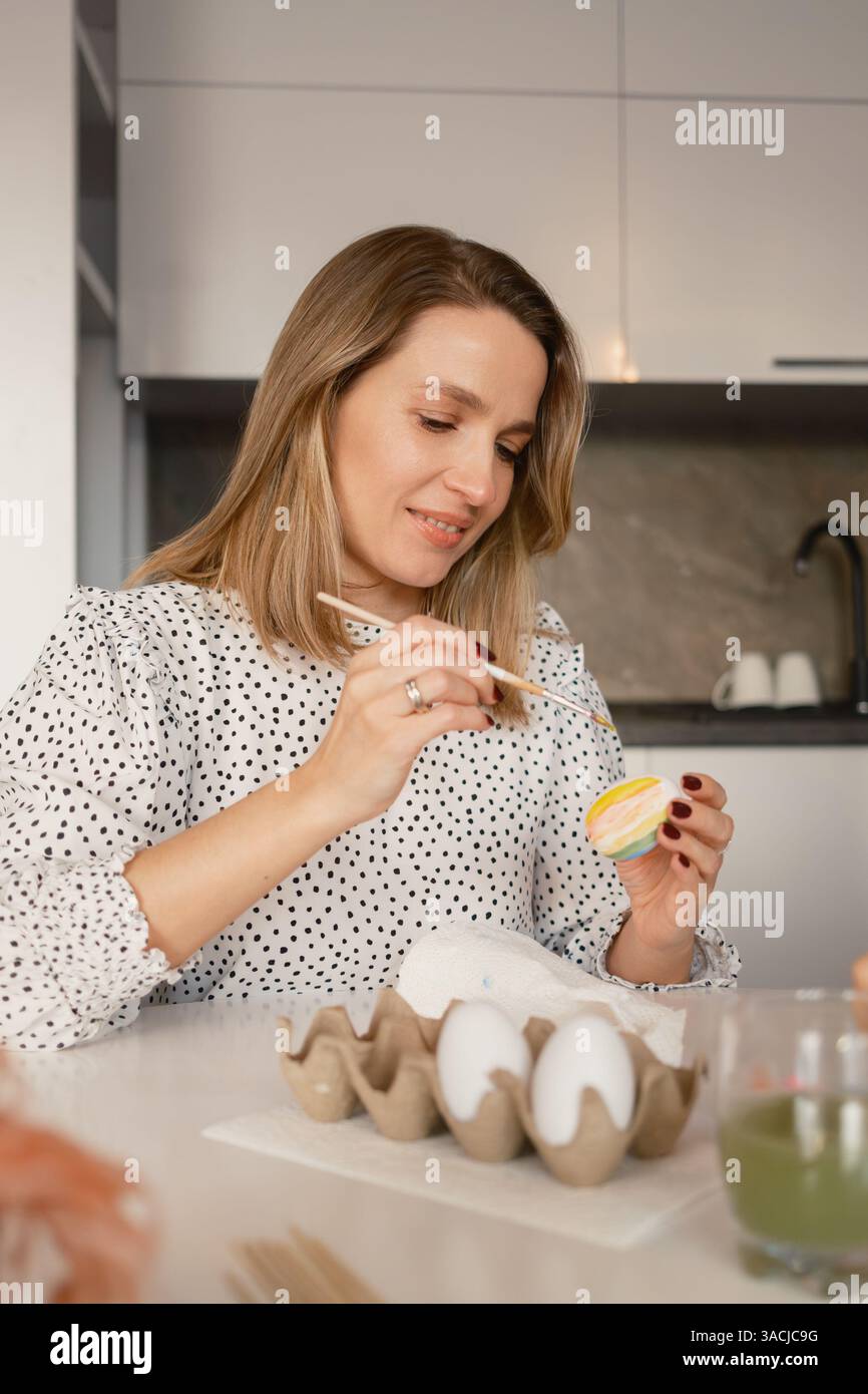 Lächelnde Frau, die Ostereier in einer gemütlichen Küche malt Stockfoto