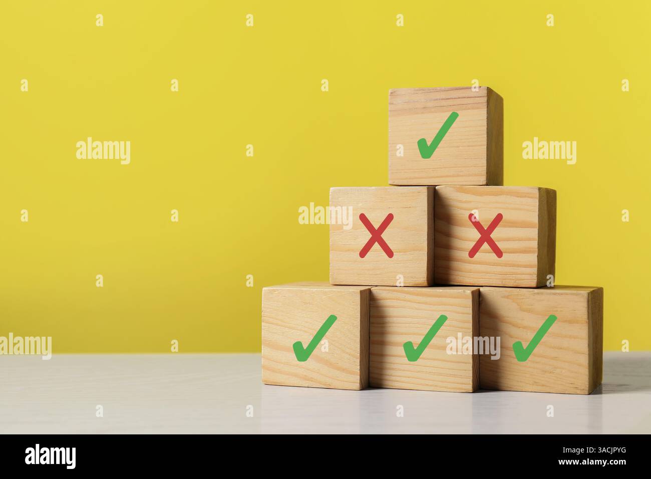 Ablehnung genehmigen. Pyramide aus Holzwürfeln mit Häkchen und Kreuzmarkierungen auf gelbem Hintergrund Stockfoto