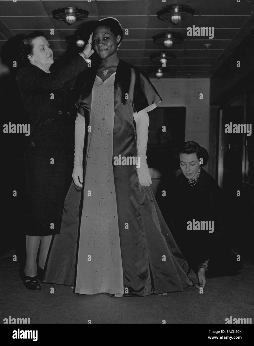 Krönungskleid einer Afrikakönigin H. M. die Königin von Buganda, die ihre Krönungssonden anzog, an denen sie an der Prozession teilnahm. Ihr Mantel ist aus blauem Satin, gefüttert mit Chartreuse-Seide; er wird über einem weißen Kleid aus Seide getragen, das mit silbernen Schnallen, Perlen und Strasssteinen besetzt ist. Ihr kleiner dreieckiger Kopfschmuck besteht aus Perlen und Topas. Abgerundet wird das Ensemble durch lange weiße Wildlederhandschuhe. Buganda ist eines der einheimischen Königreiche der Kolonie und des Protektorats Uganda in Zentralafrika. Juni 1953. (Foto: Peter J Abbey/Fairfax Media) Stockfoto