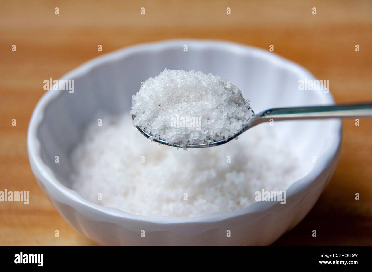 Nahaufnahme eines mit grobem Salz gefüllten Löffels, der über einer weißen Schüssel mit mehr Salz gehalten wird. Stockfoto
