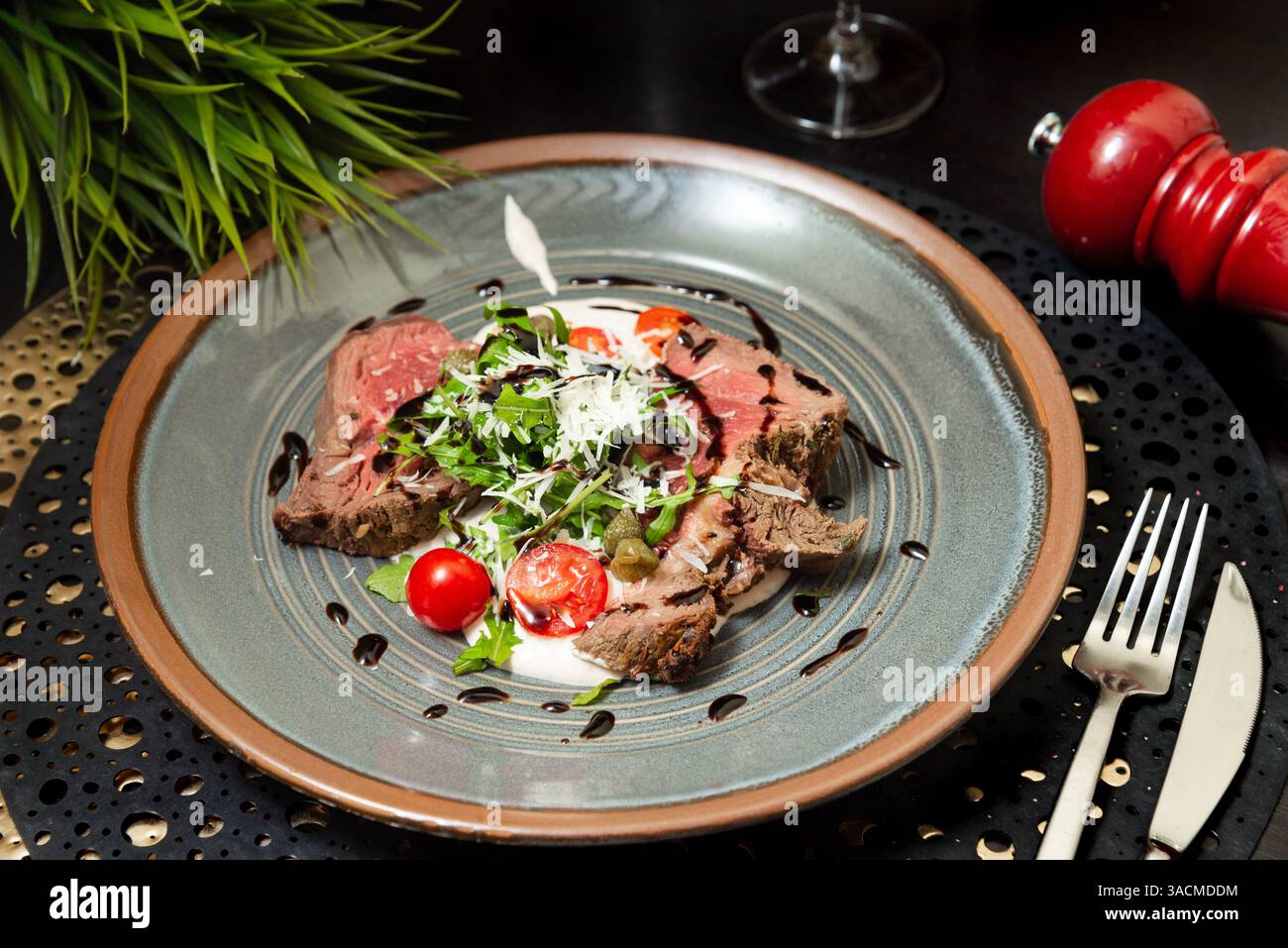 Gourmet-Gericht mit mittelseltenem Roastbeef, garniert mit Rucola, Kirschtomaten, Kapern und Parmesan, mit Balsamico-Glasur. Stockfoto