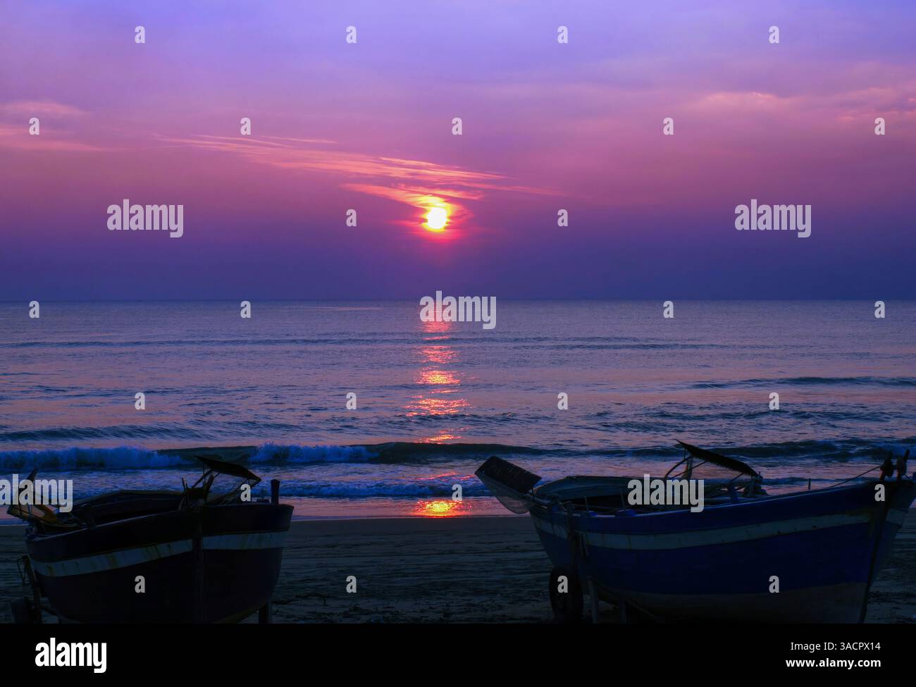 Zwei Fischerboote parken am Strand während eines pulsierenden Sonnenuntergangs, was eine ruhige und malerische Szene schafft Stockfoto