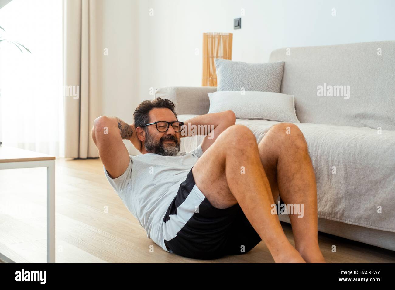 Ein erwachsener Mann von 50 Jahren, der zu Hause trainieren und Kraftübungen mit Fitnessgeräten wie Kurzhanteln und Widerstandsbändern durchführt, um sein körperliches und geistiges Wohlbefinden zu erhalten Stockfoto