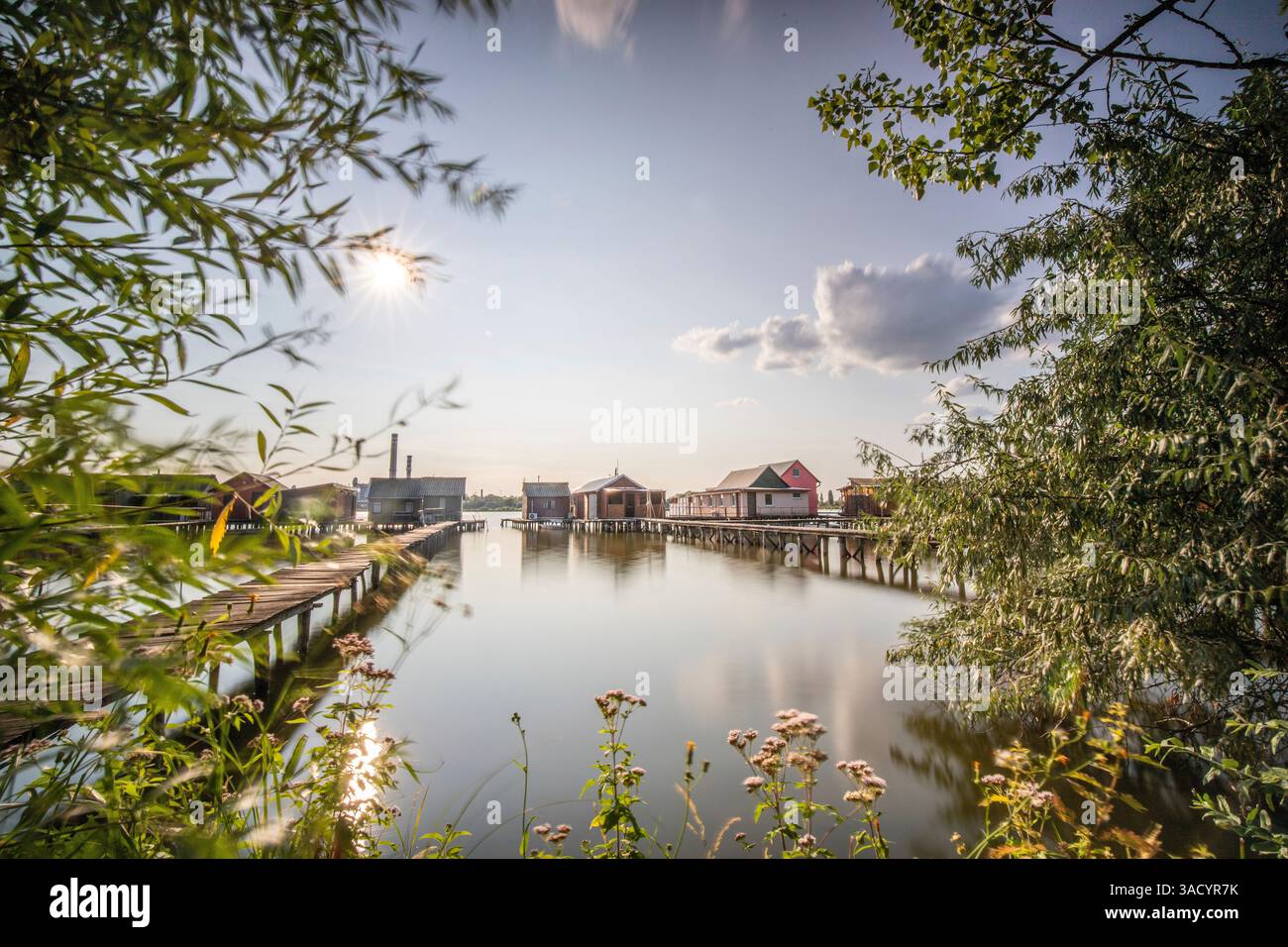 Holzhäuser im Wasser. Ferienanlage am See bei Sonnenuntergang. Lange Holzstege führen zu den einzelnen Häusern. Landschaftsaufnahme des schwimmenden Dorfes Bokodi am Balaton, Ungarn Stockfoto