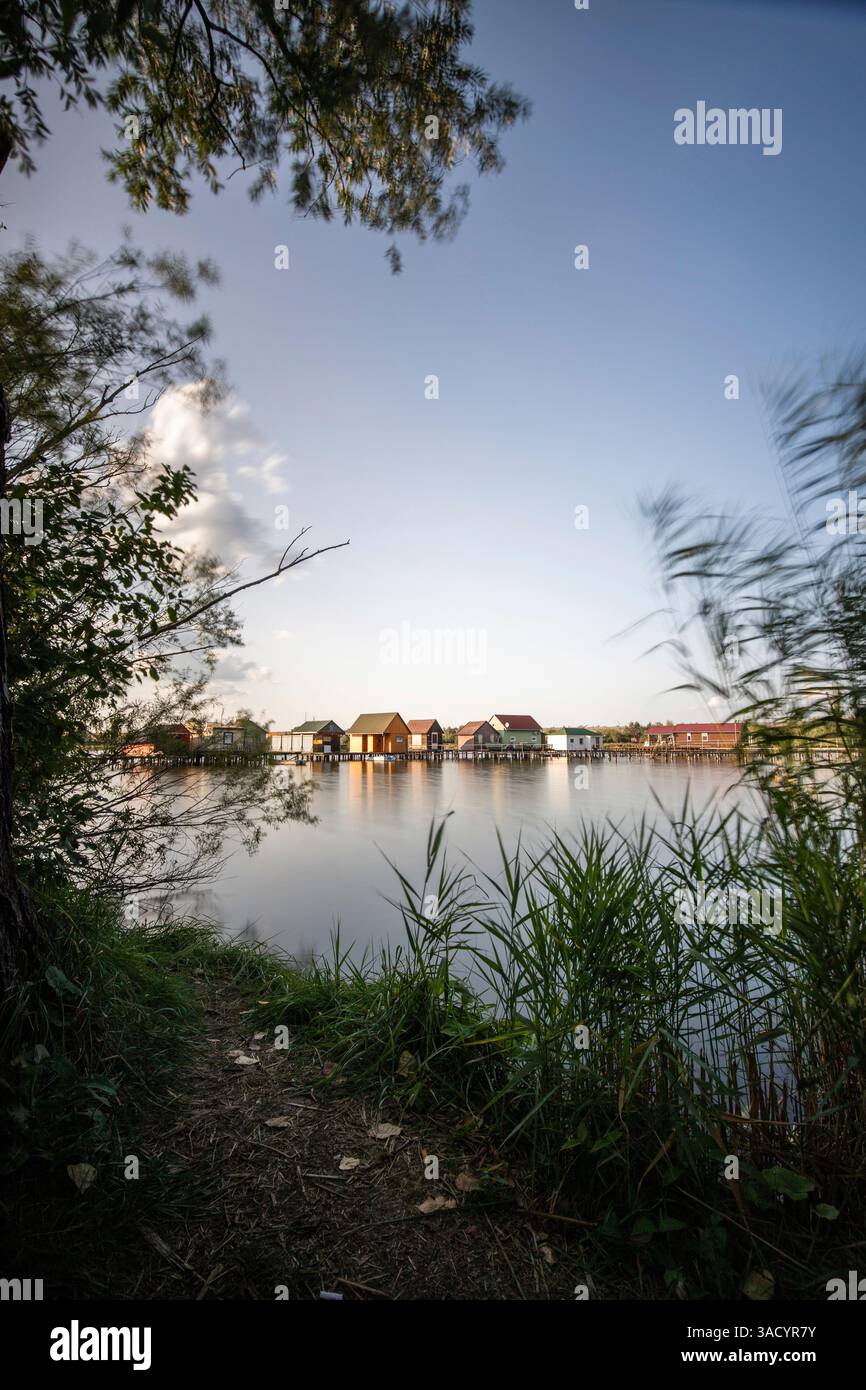 Holzhäuser im Wasser. Ferienanlage am See bei Sonnenuntergang. Lange Holzstege führen zu den einzelnen Häusern. Landschaftsaufnahme des schwimmenden Dorfes Bokodi am Balaton, Ungarn Stockfoto