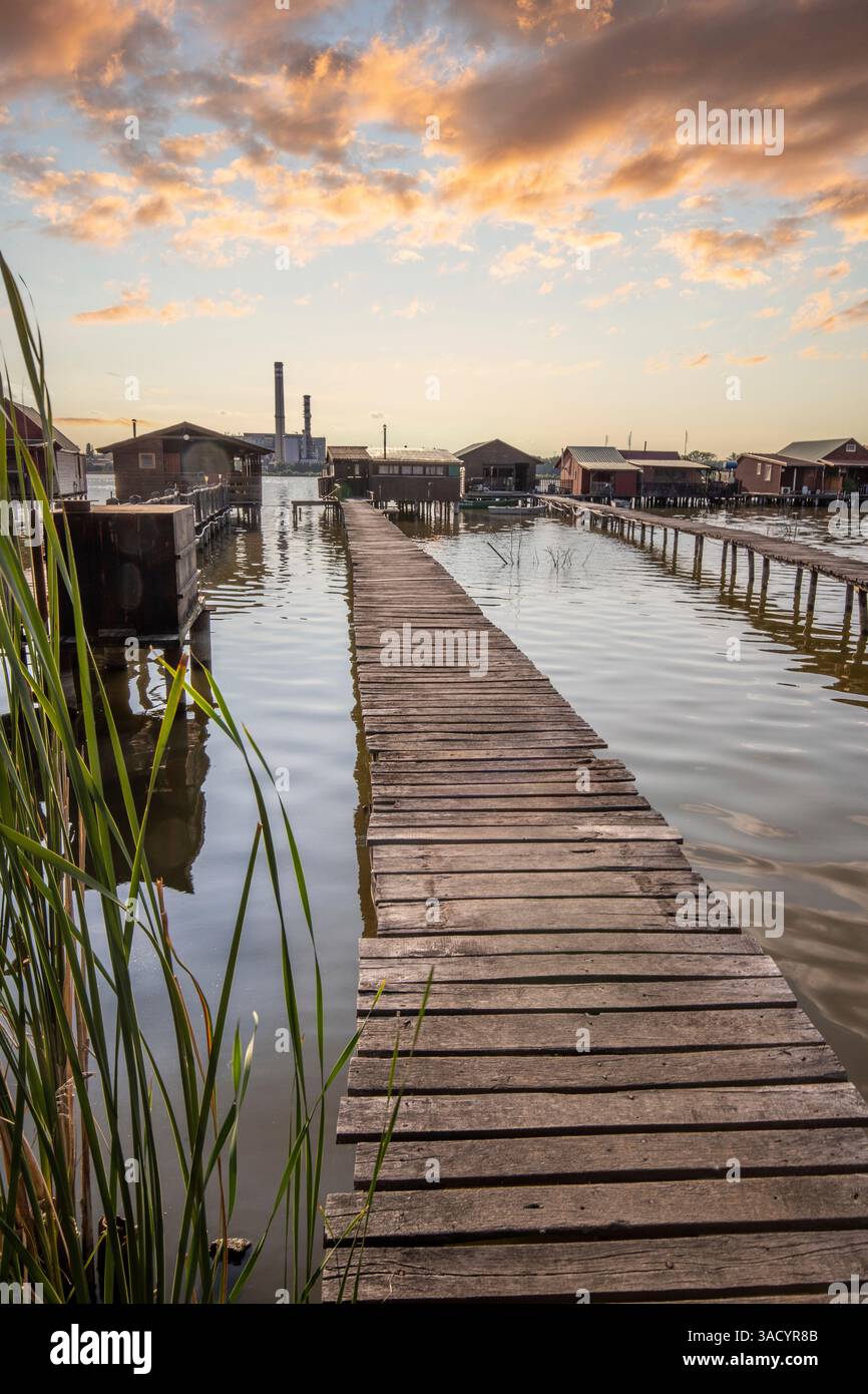 Holzhäuser im Wasser. Ferienanlage am See bei Sonnenuntergang. Lange Holzstege führen zu den einzelnen Häusern. Landschaftsaufnahme des schwimmenden Dorfes Bokodi am Balaton, Ungarn Stockfoto