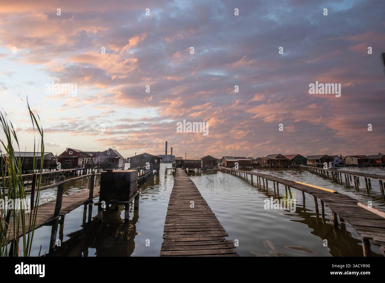 Holzhäuser im Wasser. Ferienanlage am See bei Sonnenuntergang. Lange Holzstege führen zu den einzelnen Häusern. Landschaftsaufnahme des schwimmenden Dorfes Bokodi am Balaton, Ungarn Stockfoto