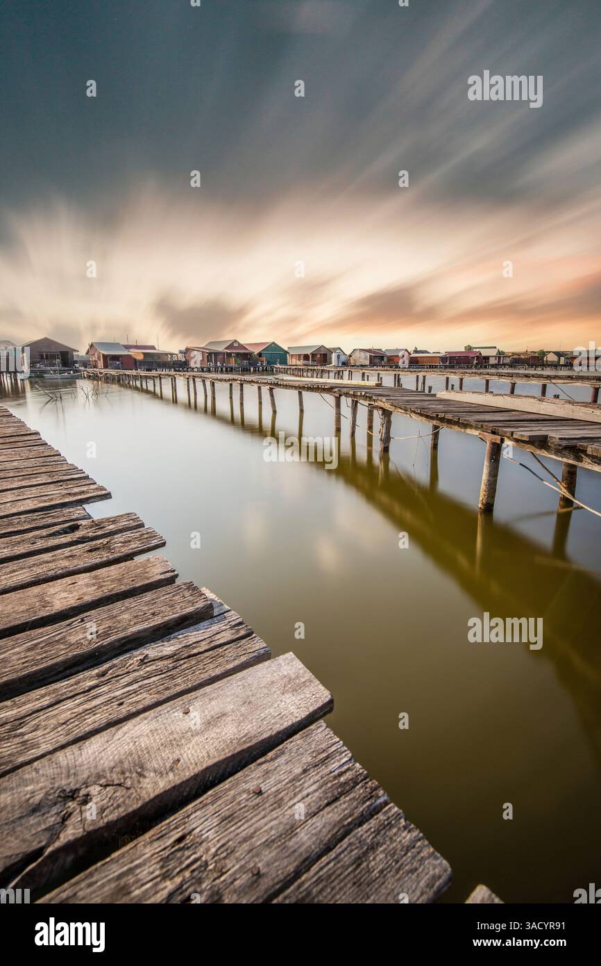 Holzhäuser im Wasser. Ferienanlage am See bei Sonnenuntergang. Lange Holzstege führen zu den einzelnen Häusern. Landschaftsaufnahme des schwimmenden Dorfes Bokodi am Balaton, Ungarn Stockfoto