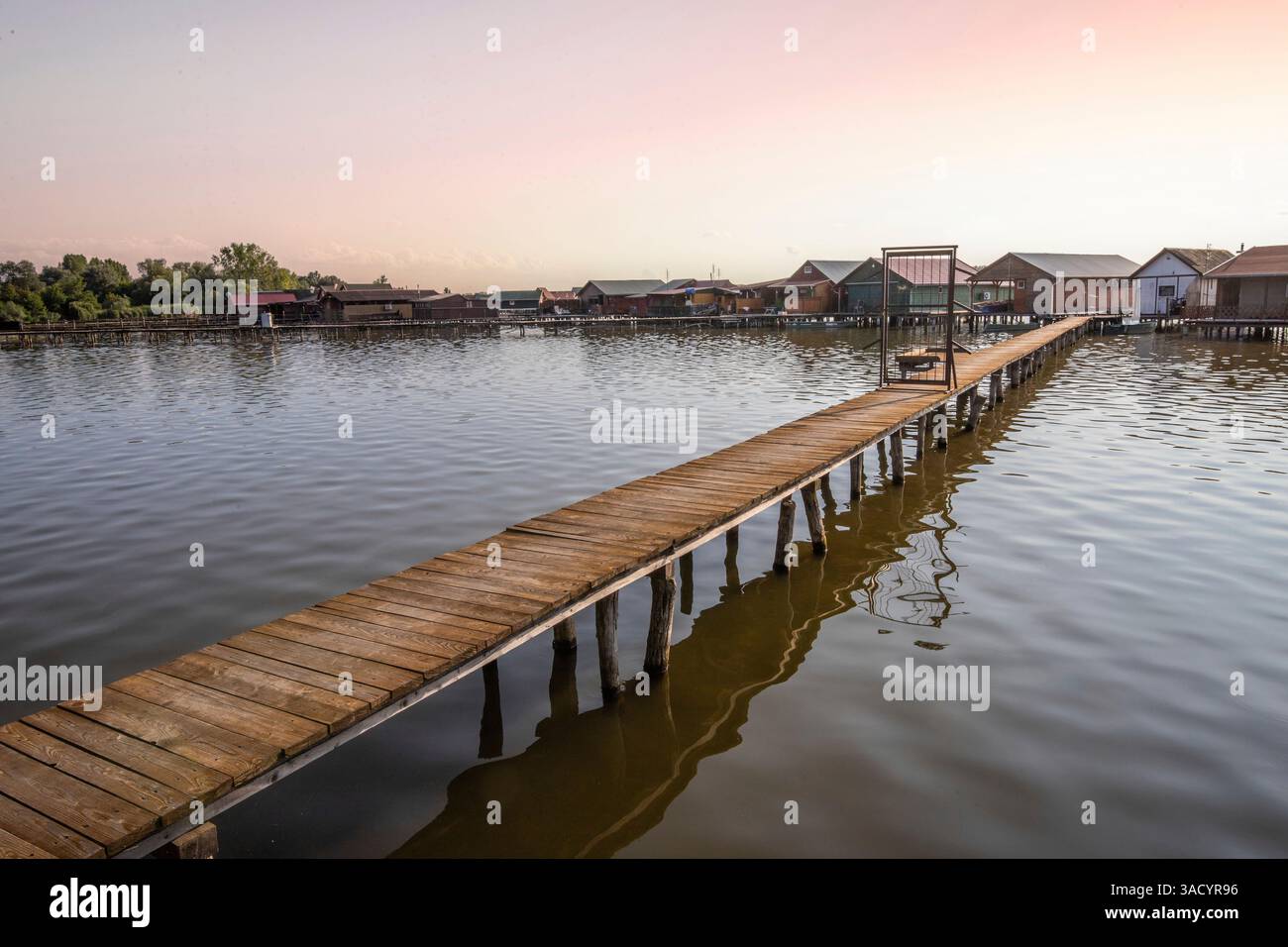 Holzhäuser im Wasser. Ferienanlage am See bei Sonnenuntergang. Lange Holzstege führen zu den einzelnen Häusern. Landschaftsaufnahme des schwimmenden Dorfes Bokodi am Balaton, Ungarn Stockfoto