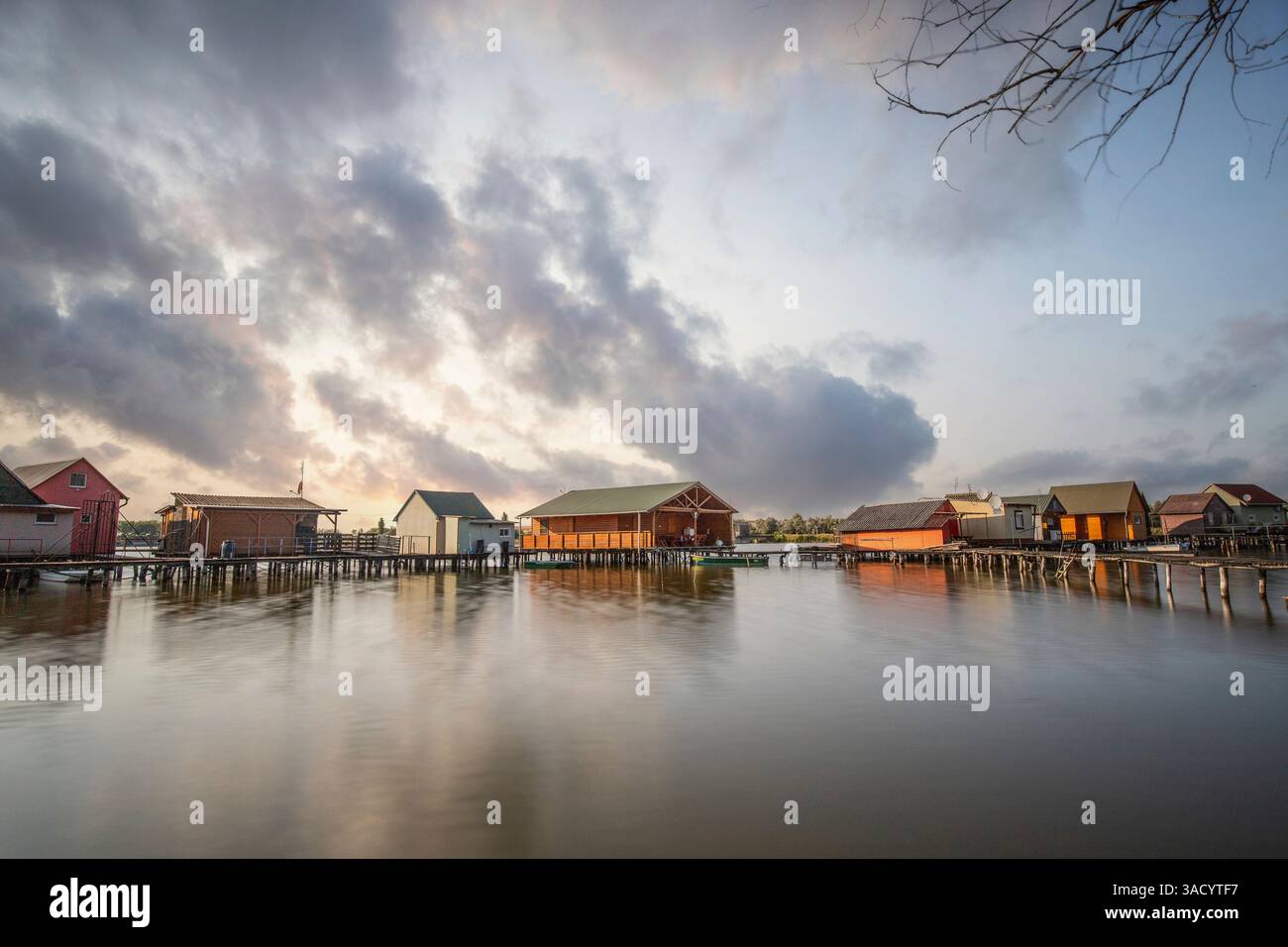 Holzhäuser im Wasser. Ferienanlage am See bei Sonnenuntergang. Lange Holzstege führen zu den einzelnen Häusern. Landschaftsaufnahme des schwimmenden Dorfes Bokodi am Balaton, Ungarn Stockfoto