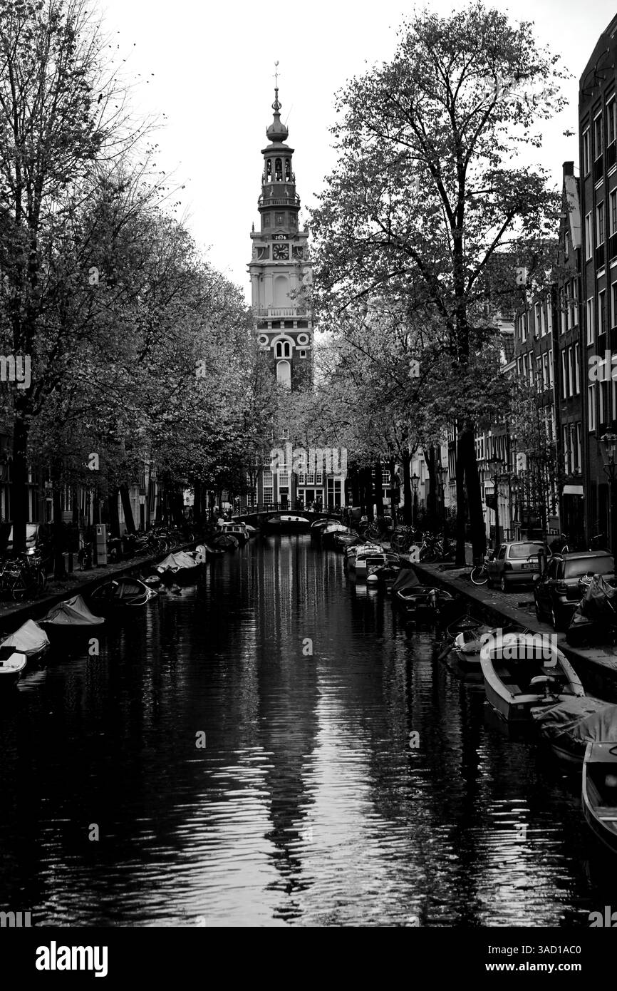 Das berühmte Zuiderkerk erhebt sich über einem ruhigen Amsterdamer Kanal, dessen Reflexion in stillen Gewässern schimmert, eingerahmt von Booten, Bäumen und historischem Charme Stockfoto