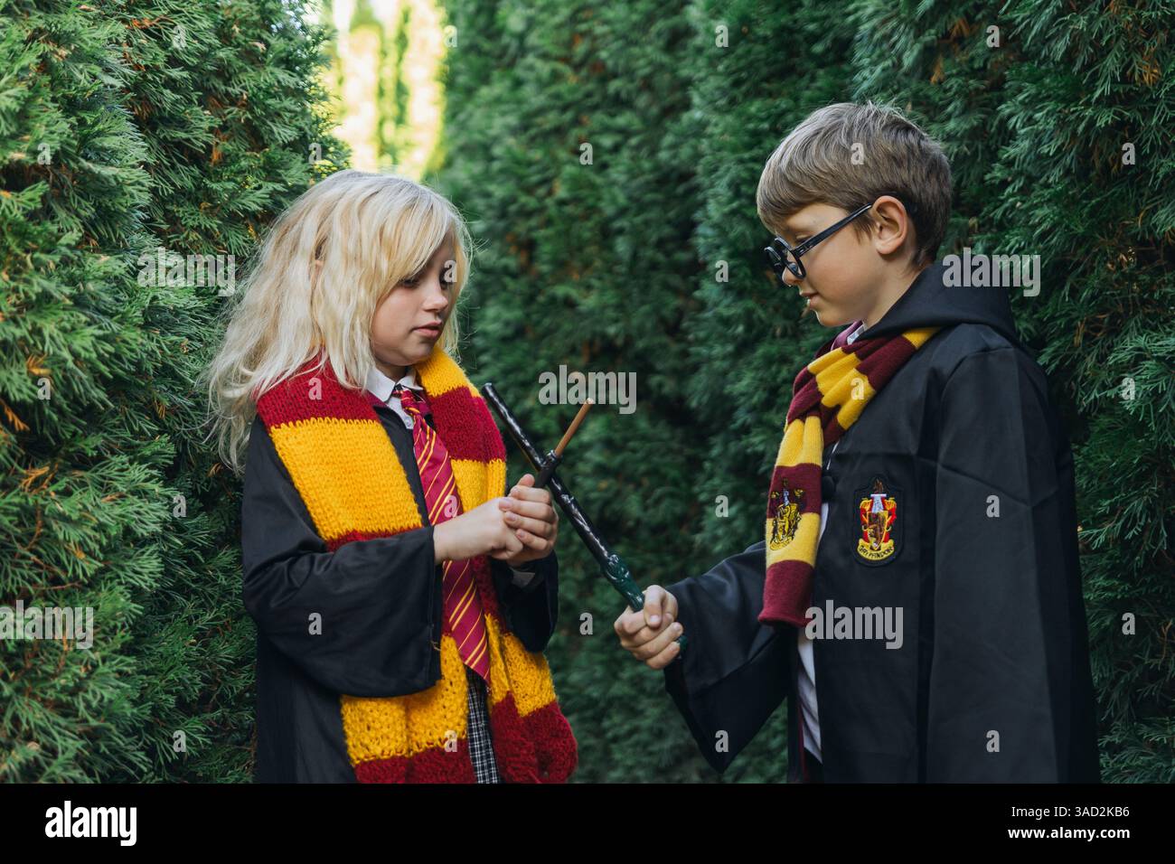Harry Potter Kostüme Kids Forest Magic – zwei Kinder, die als Harry Potter-Figuren verkleidet sind, stehen in einem Wald und halten einen Stab. Stockfoto