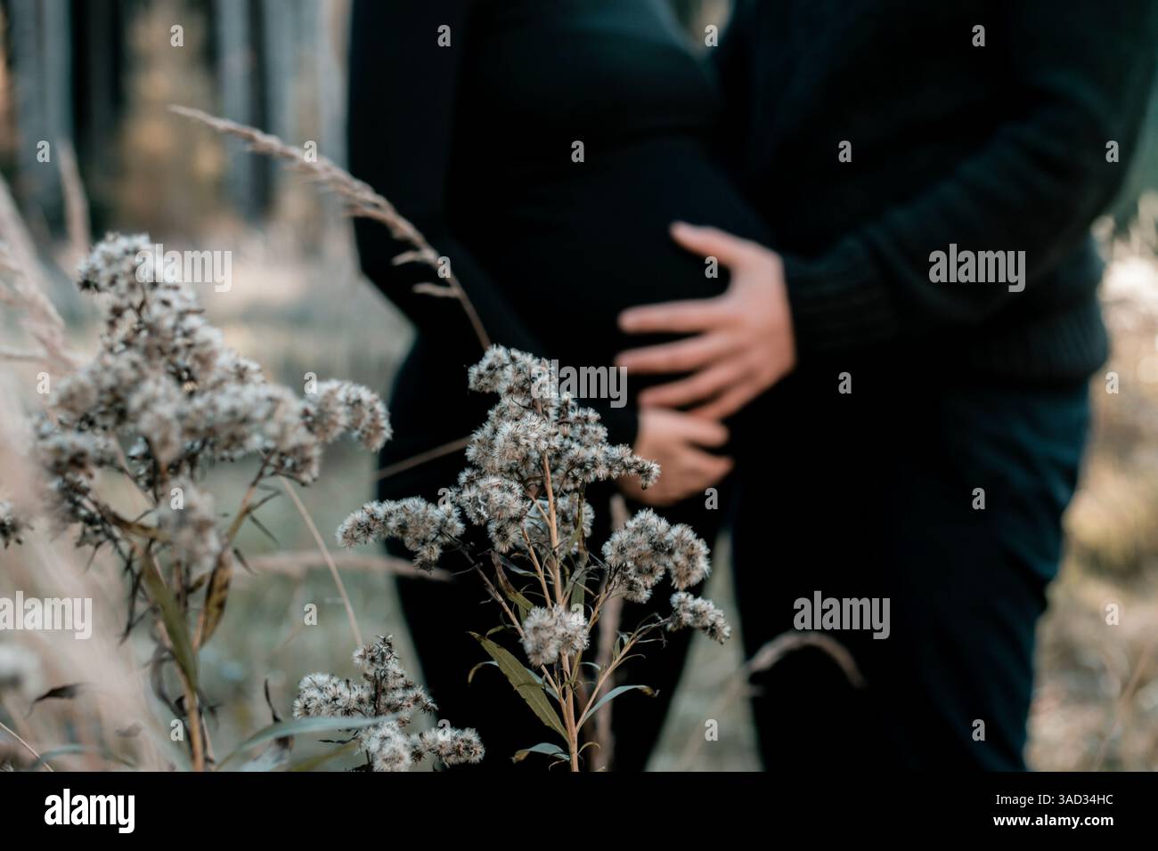 Ein Paar, das auf einem Feld steht, ein Mann, der die Babypuppe der Frau schützend hält, beide tragen schwarze Kleidung, Babypuppen schießen, Herbst Stockfoto