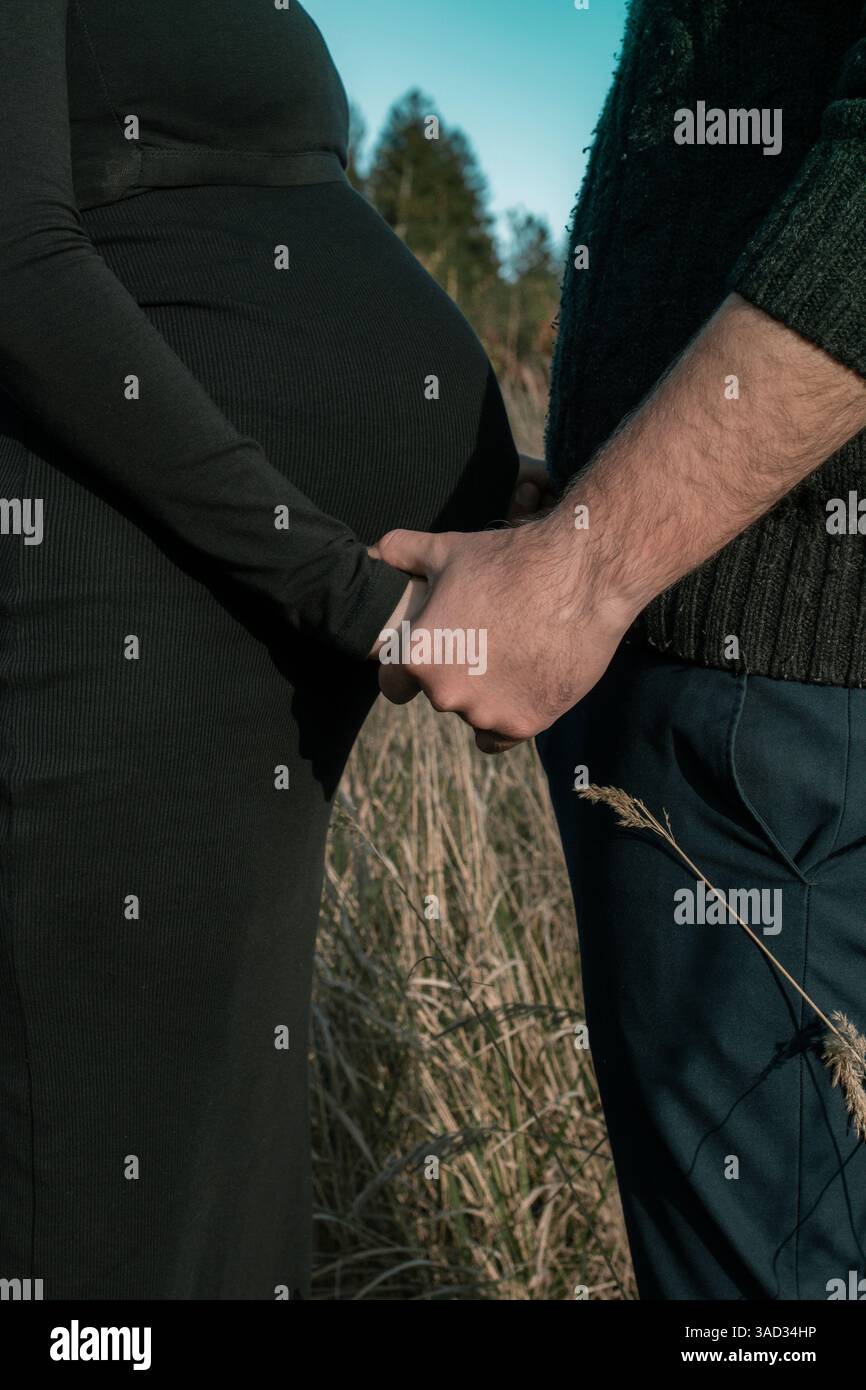 Paare beim Baby-Shooting, Hände halten, schützende Geste, Vater und Mutter stehen auf einem Feld Stockfoto