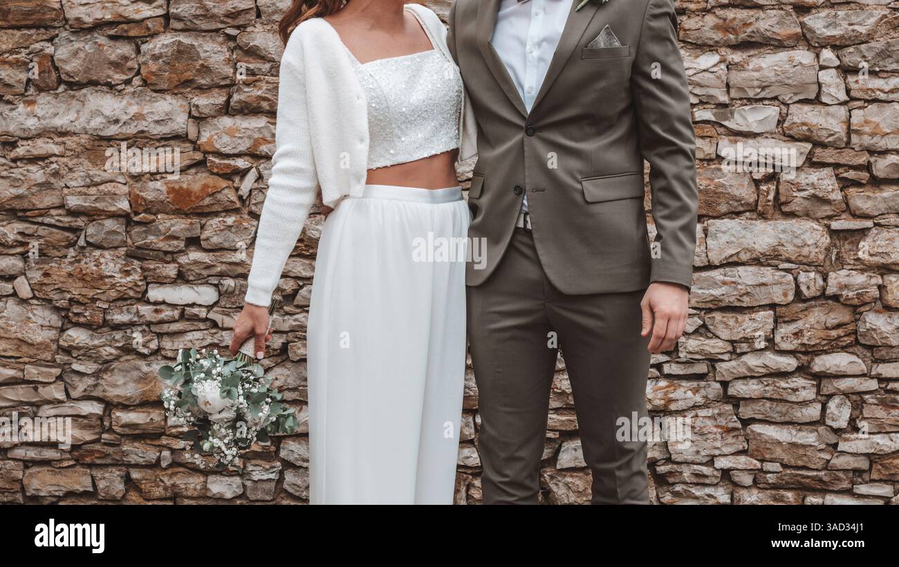 Braut und Bräutigam stehen nebeneinander, Braut trägt einen bauchigen Hosenanzug anstelle eines Kleides im Standesamt, ein Paar hält Hände Stockfoto