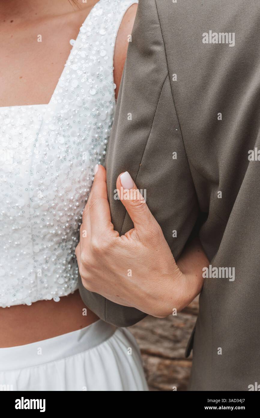 Braut und Bräutigam stehen nebeneinander, Braut trägt einen bauchigen Hosenanzug statt eines Kleides im Standesamt, Arm in Arm, Nahaufnahme, Detail Stockfoto