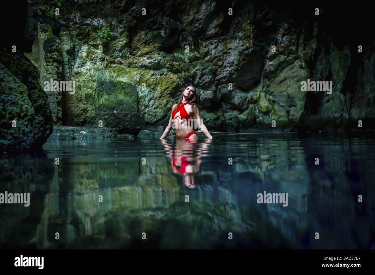 In Cuzama, Yucatan, Mexiko, schwelgt ein atemberaubendes Modell in den leuchtenden Farben des blauen und grünen Wassers eines Cenoten und schafft so eine malerische Szene des natürlichen B Stockfoto