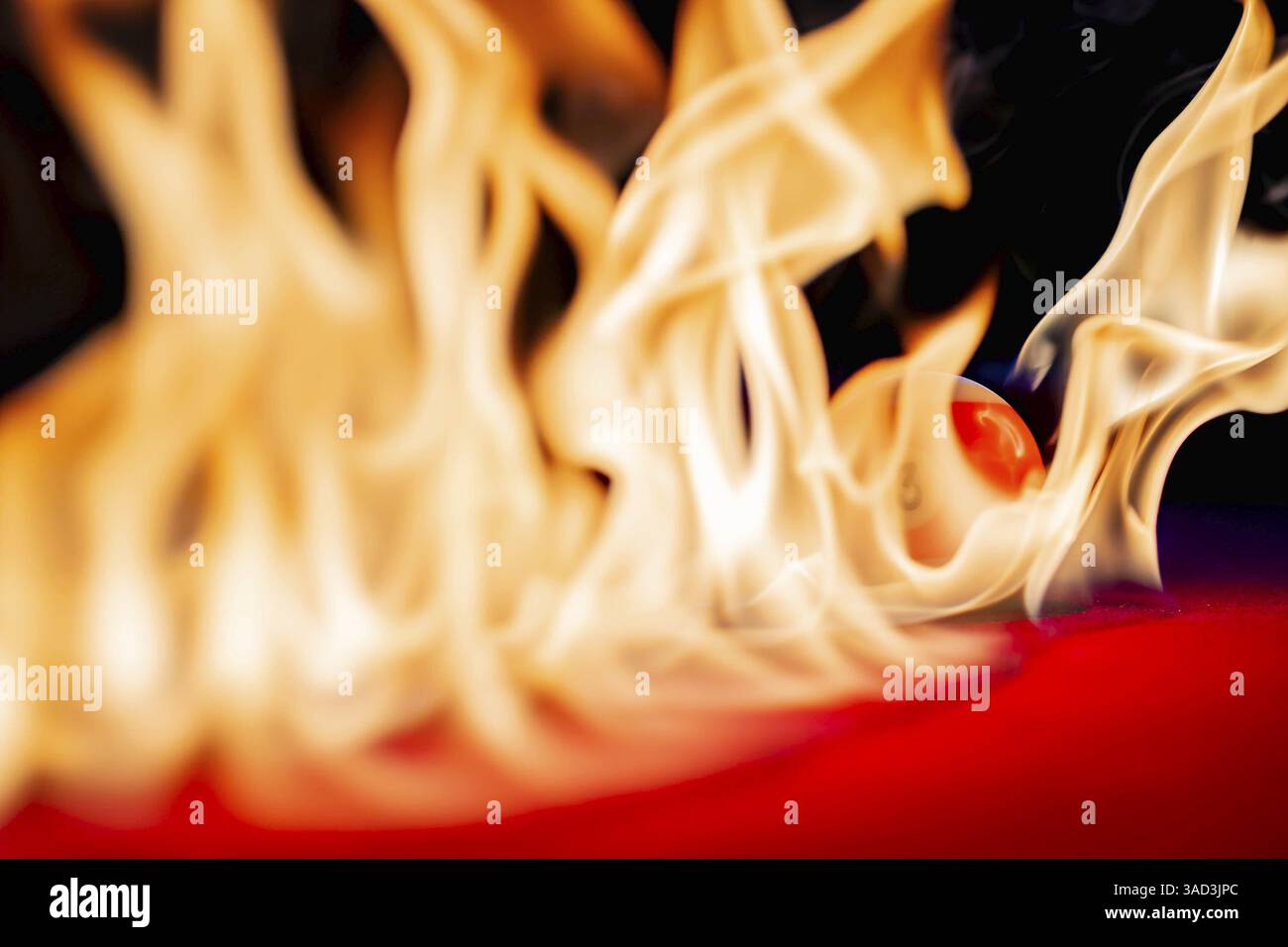 Ein Billardtisch ist von Flammen umgeben, mit glühenden Kugeln, die sich über den verkohlten roten Filz verstreuen. Rauch kräuselt sich nach oben und wirft unheimliche Schatten, wie jeder Stockfoto