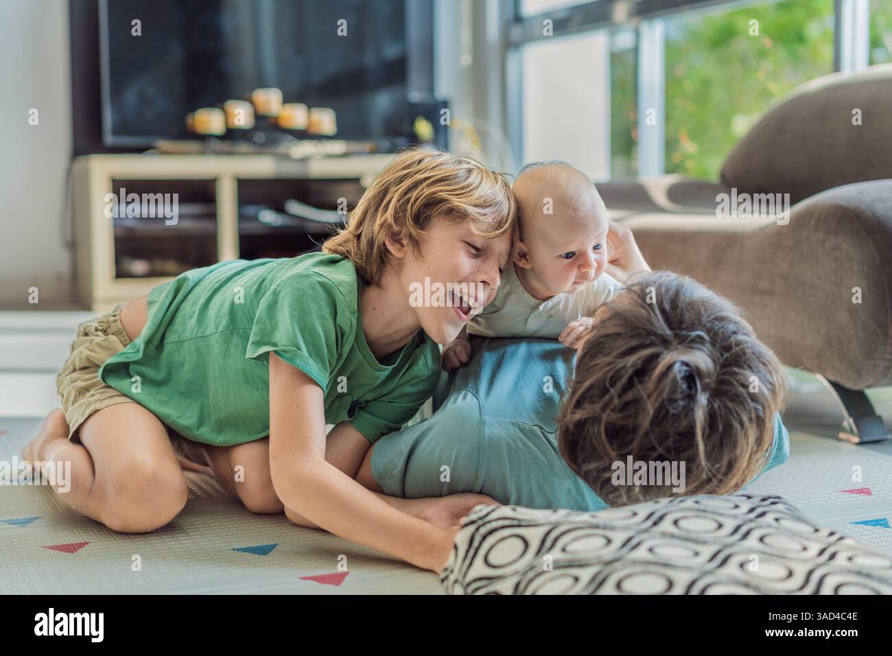 Vater, Sohn und neugeborenes Baby liegen auf dem Boden in einem gemütlichen Kinderzimmer und feiern die Ankunft ihres neuesten Familienmitglieds. Elternschaft, Bindung und Stockfoto
